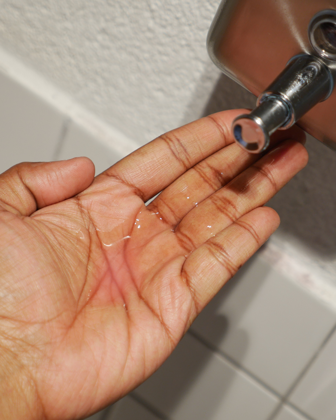 Hand under a hand soap dispenser filled with pink liquid soap