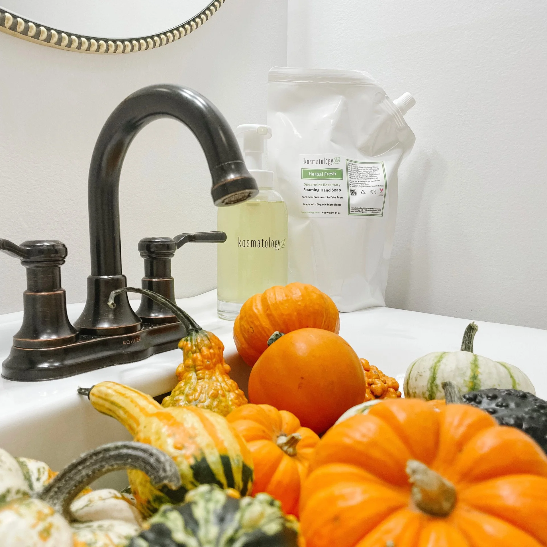 Kosmatology Herbal Fresh hand soap refill with glass bottle next to a sink full of pumpkins