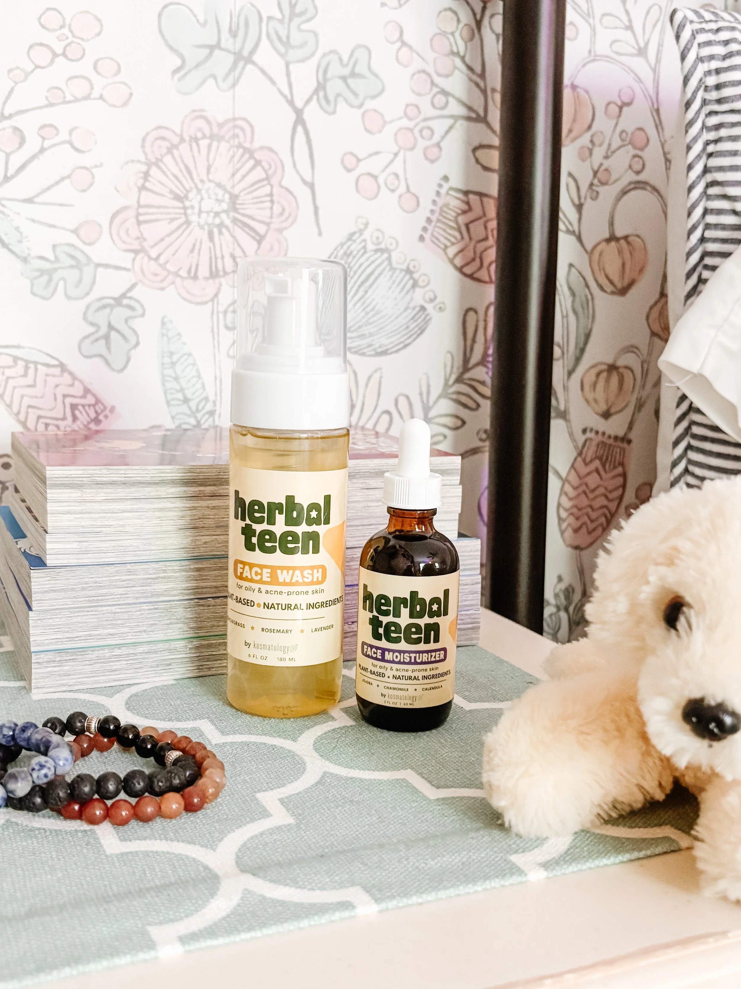 Herbal Teen face wash and moisturizer by Kosmatology on a nightstand with stuffed animals and bracelets.