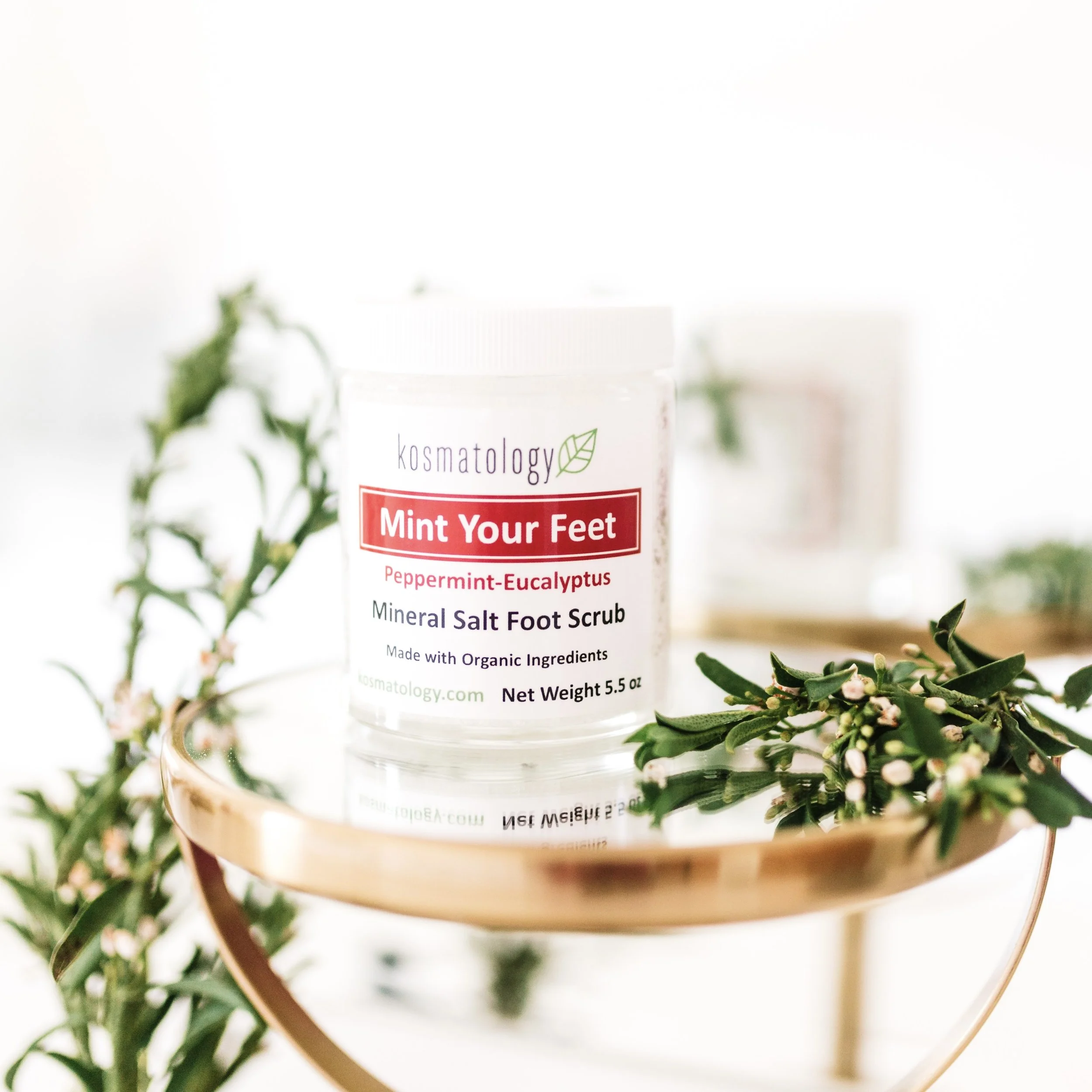 Kosmatology Mint Your Feet salt scrub on a mirrored tray surrounded by herbs