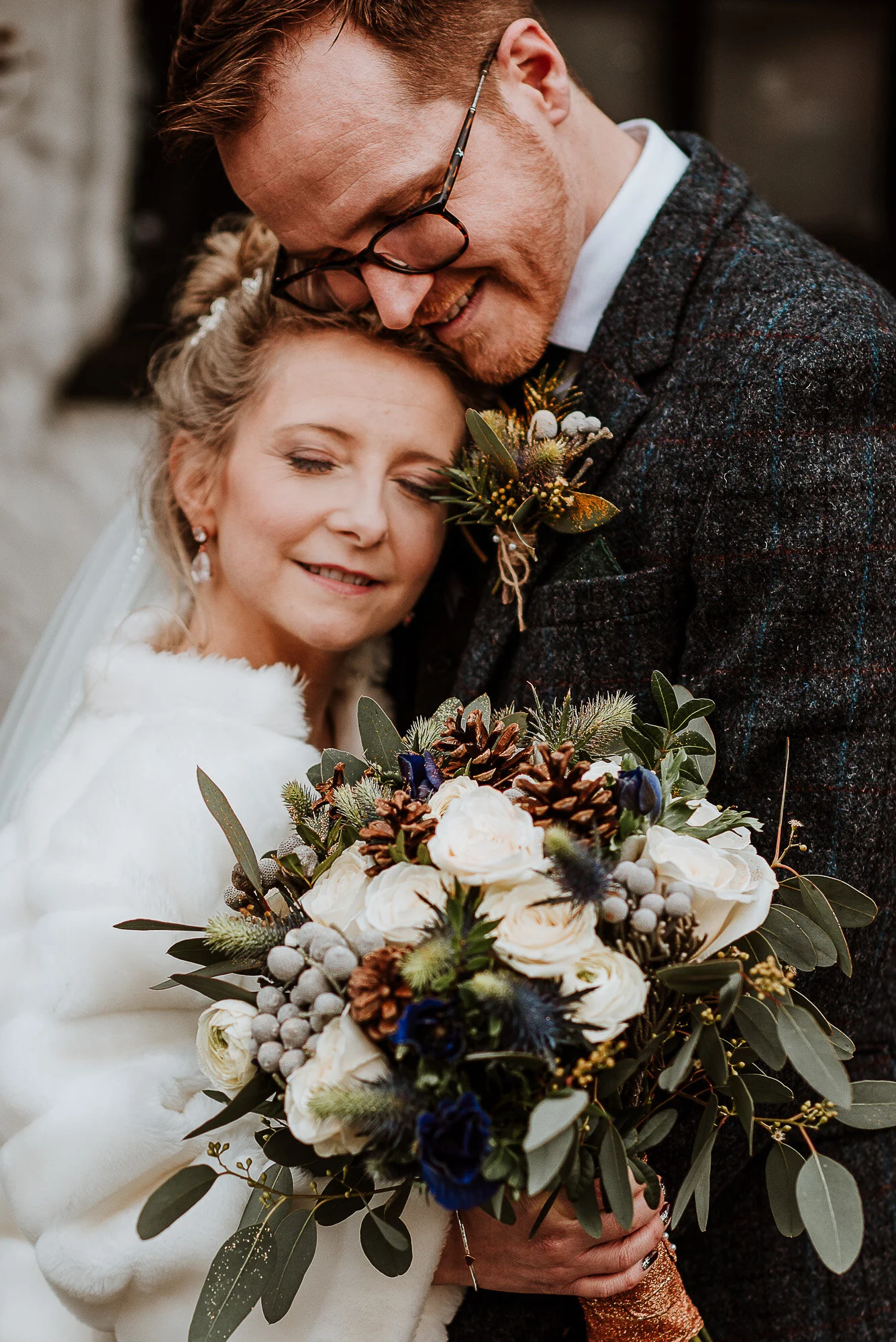 Bride and groom embracing with a winter-themed bouquet