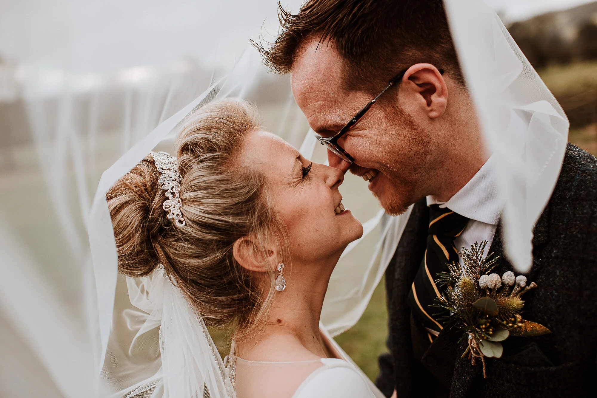 A bride and groom smiling under a veil during their wedding.