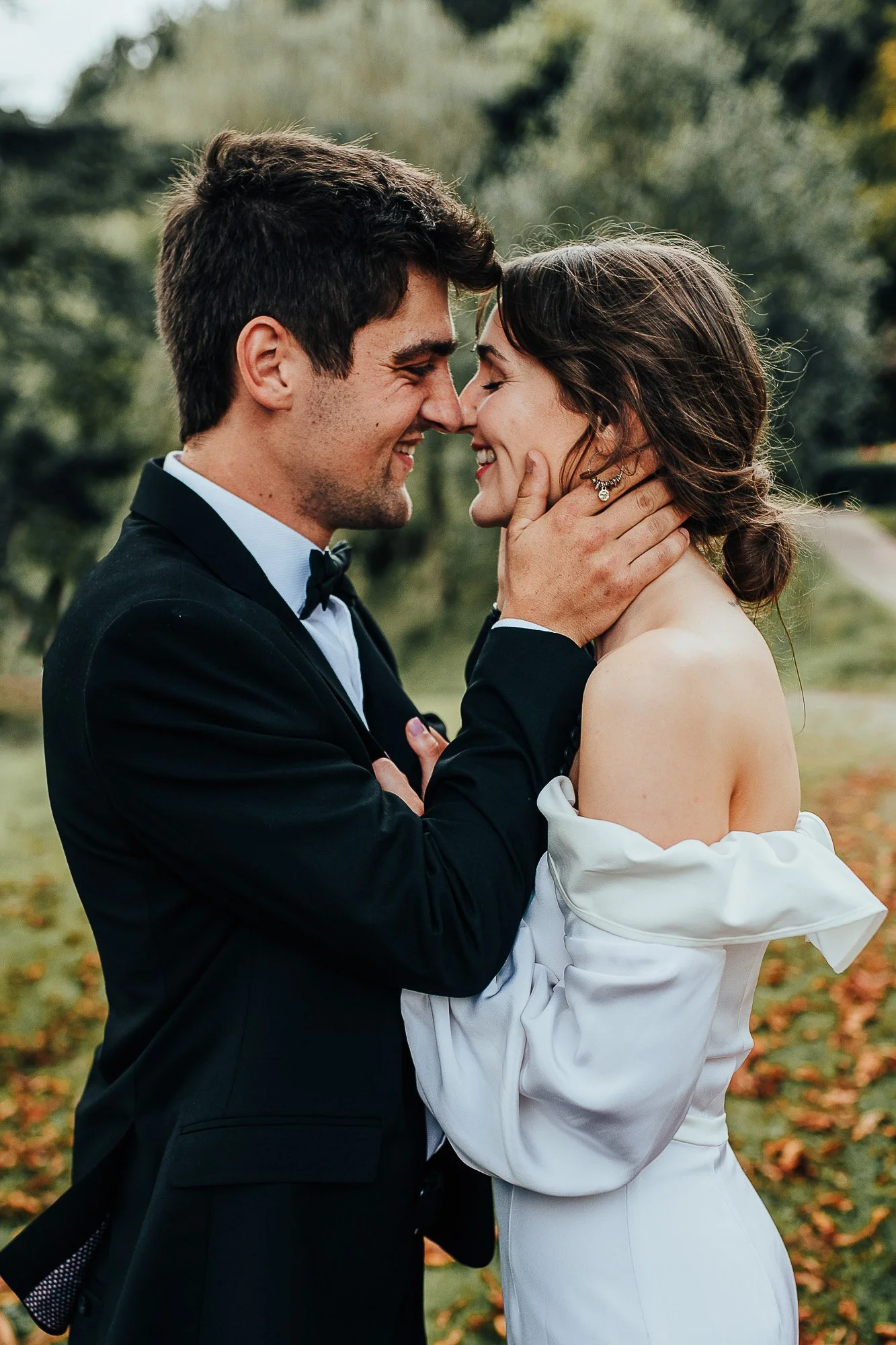 A couple in formal attire embracing outdoors, smiling at each other.