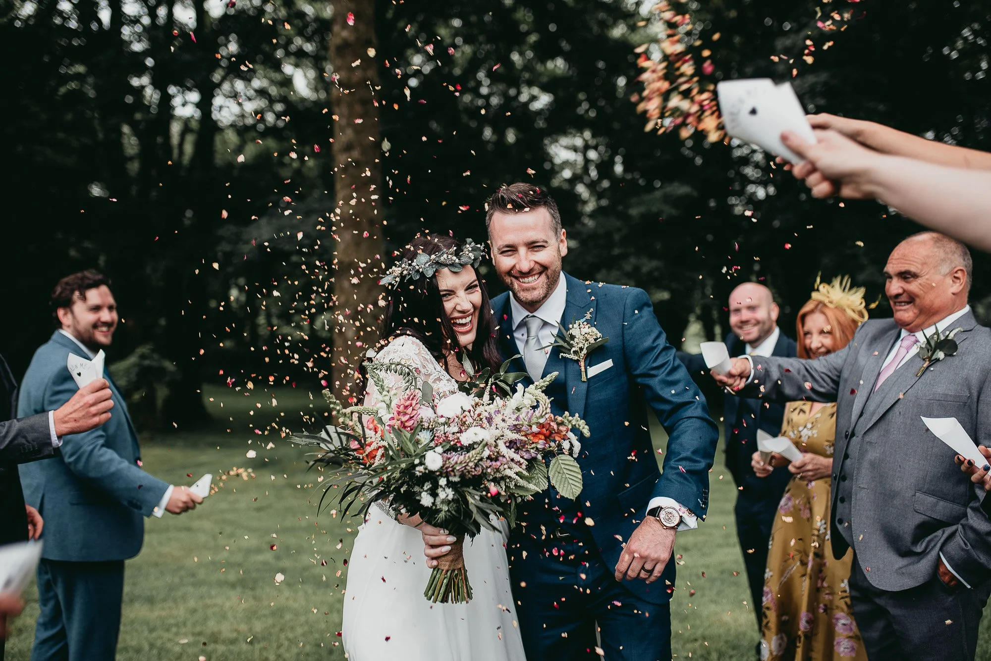 Bride and groom walking through confetti shower, surrounded by smiling wedding guests.
