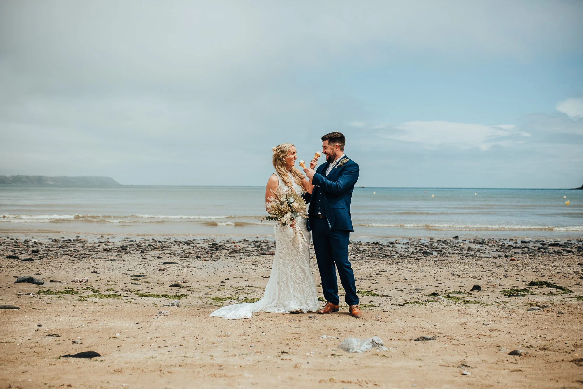 Bride and groom on a beach holding ice cream cones.