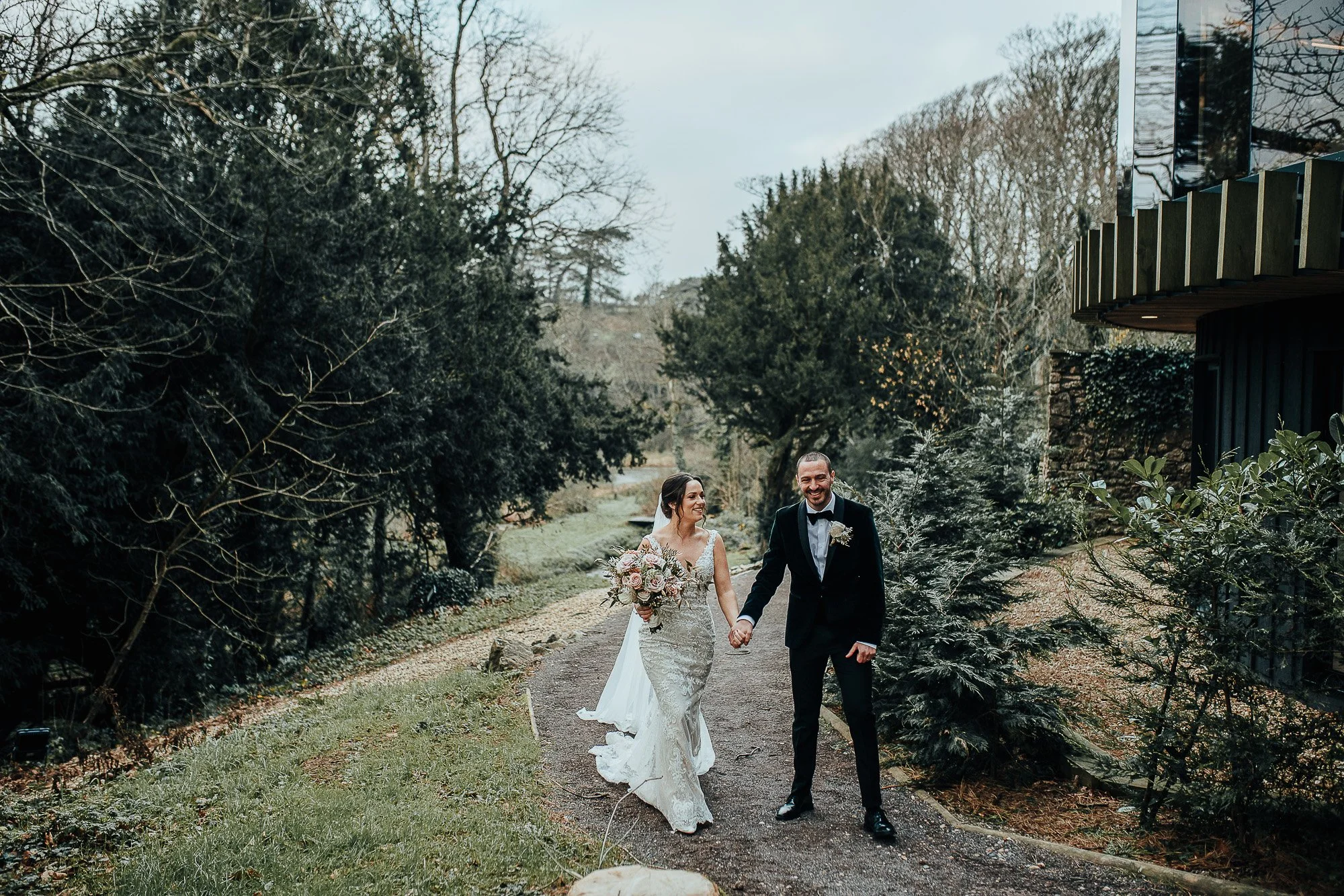 Bride and groom walking in a garden, bride holding bouquet, smiling.