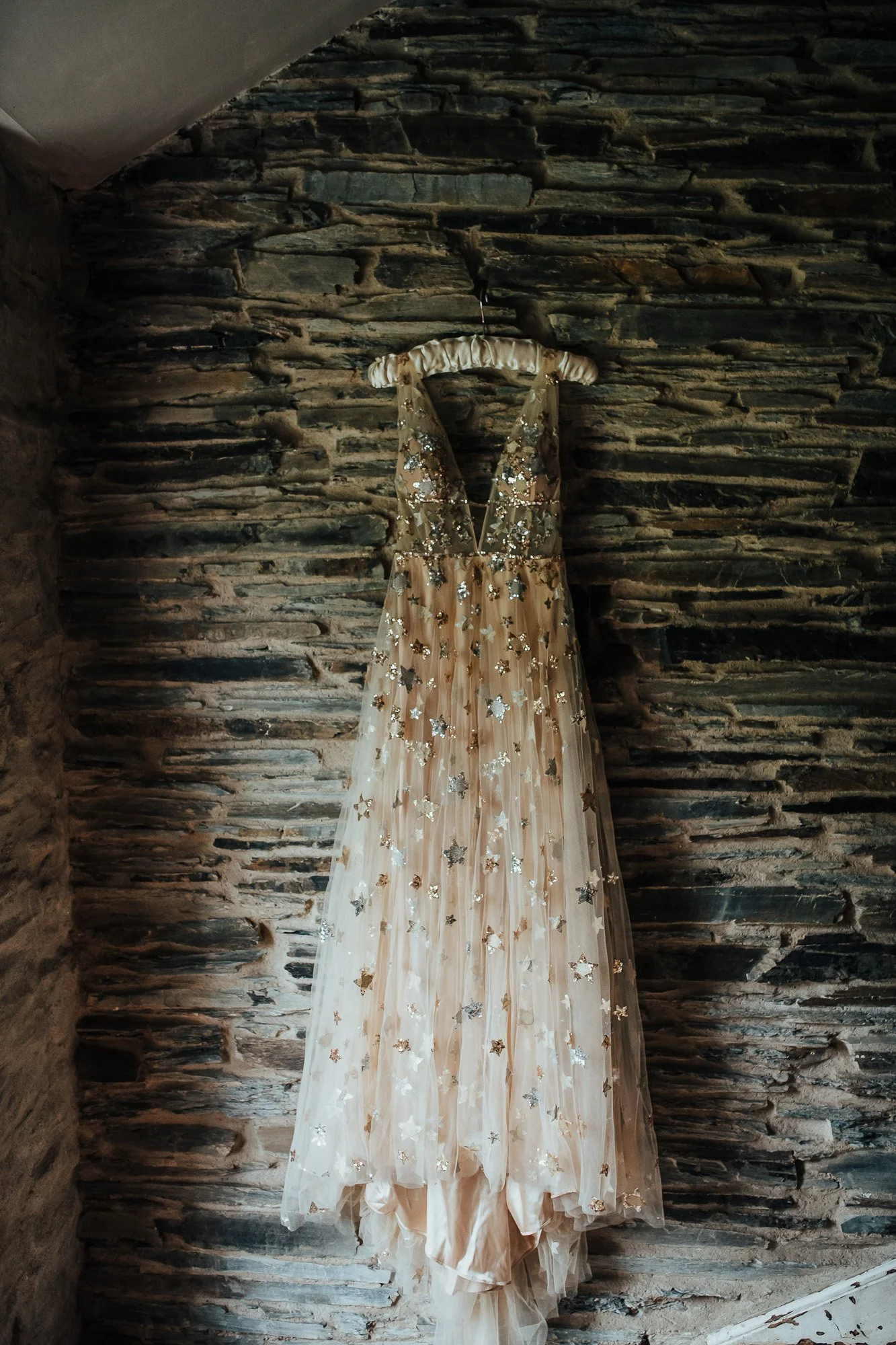 A beaded gown with star embellishments hanging on a stone wall.