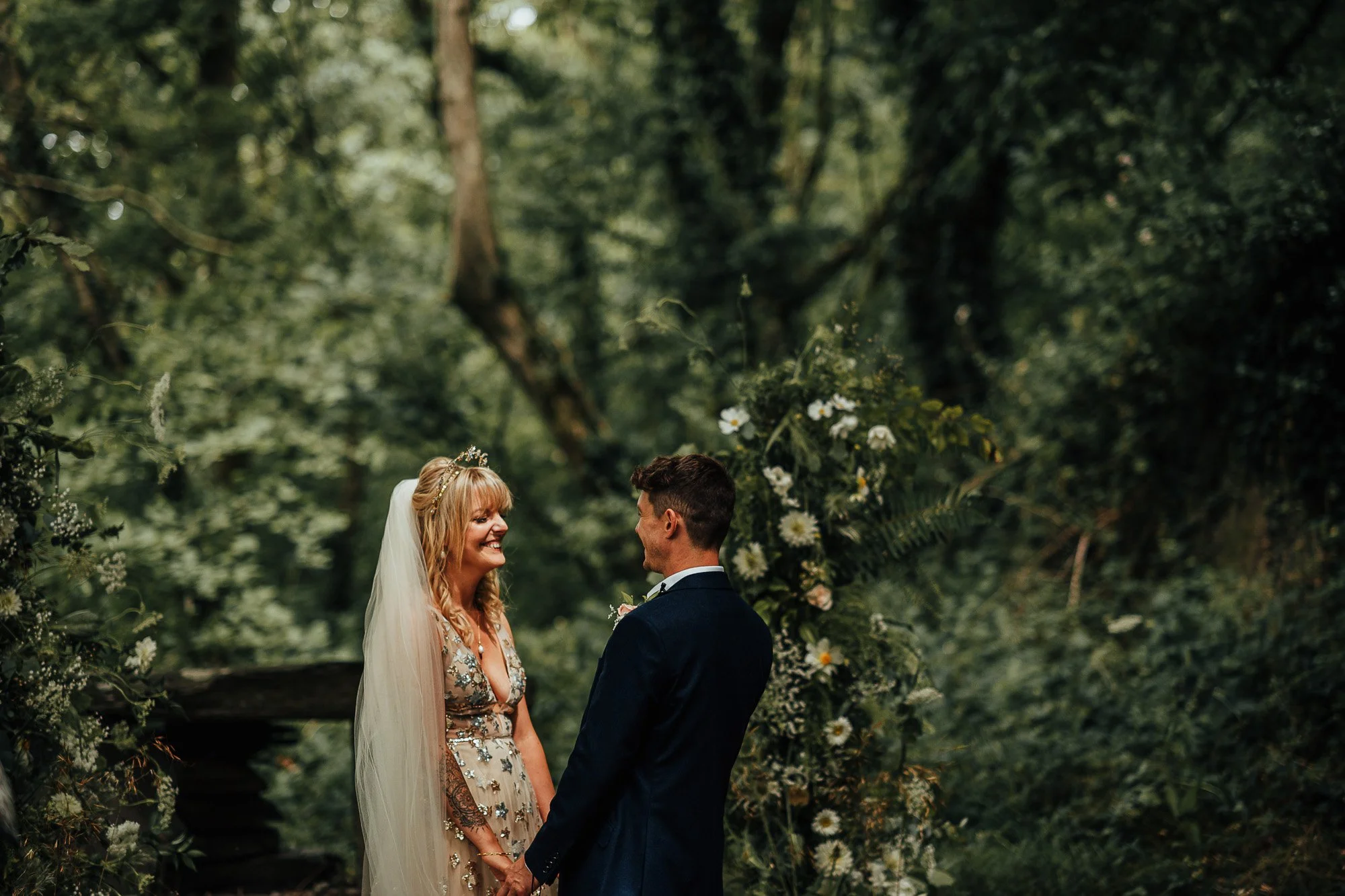 Bride and groom holding hands in a forest setting during wedding ceremony.