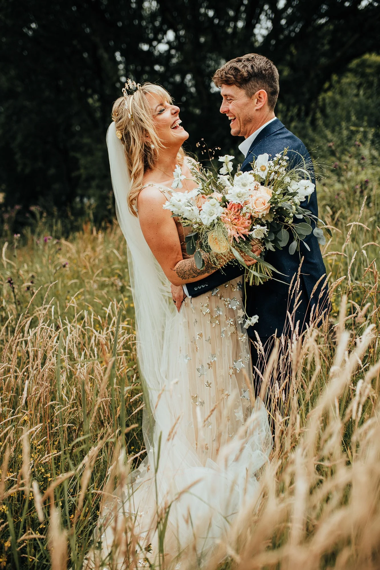 Bride and groom smiling in a field, bride holding a bouquet of flowers.