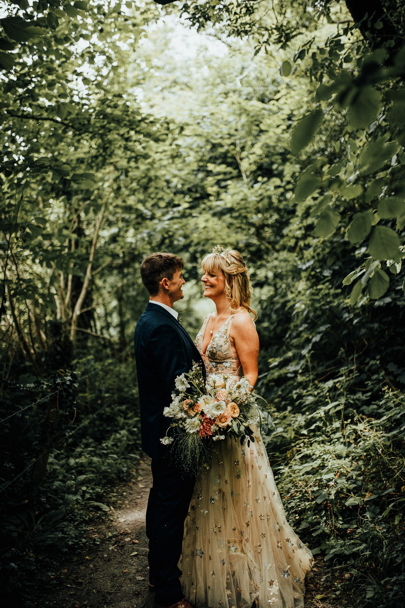 Bride and groom standing in a lush forest, the bride holding a bouquet of flowers.