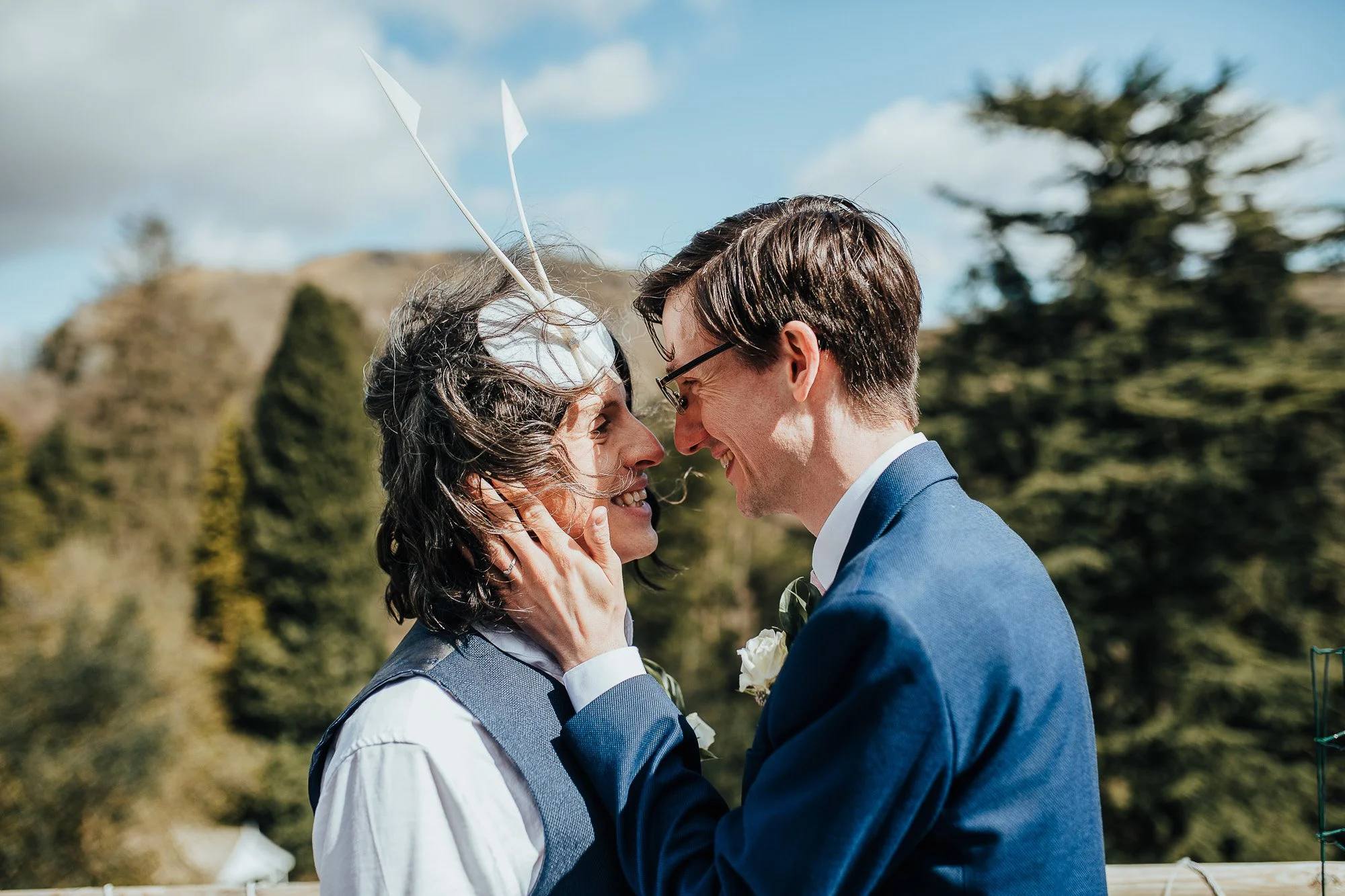 Two people in suits embracing outdoors with trees in the background.