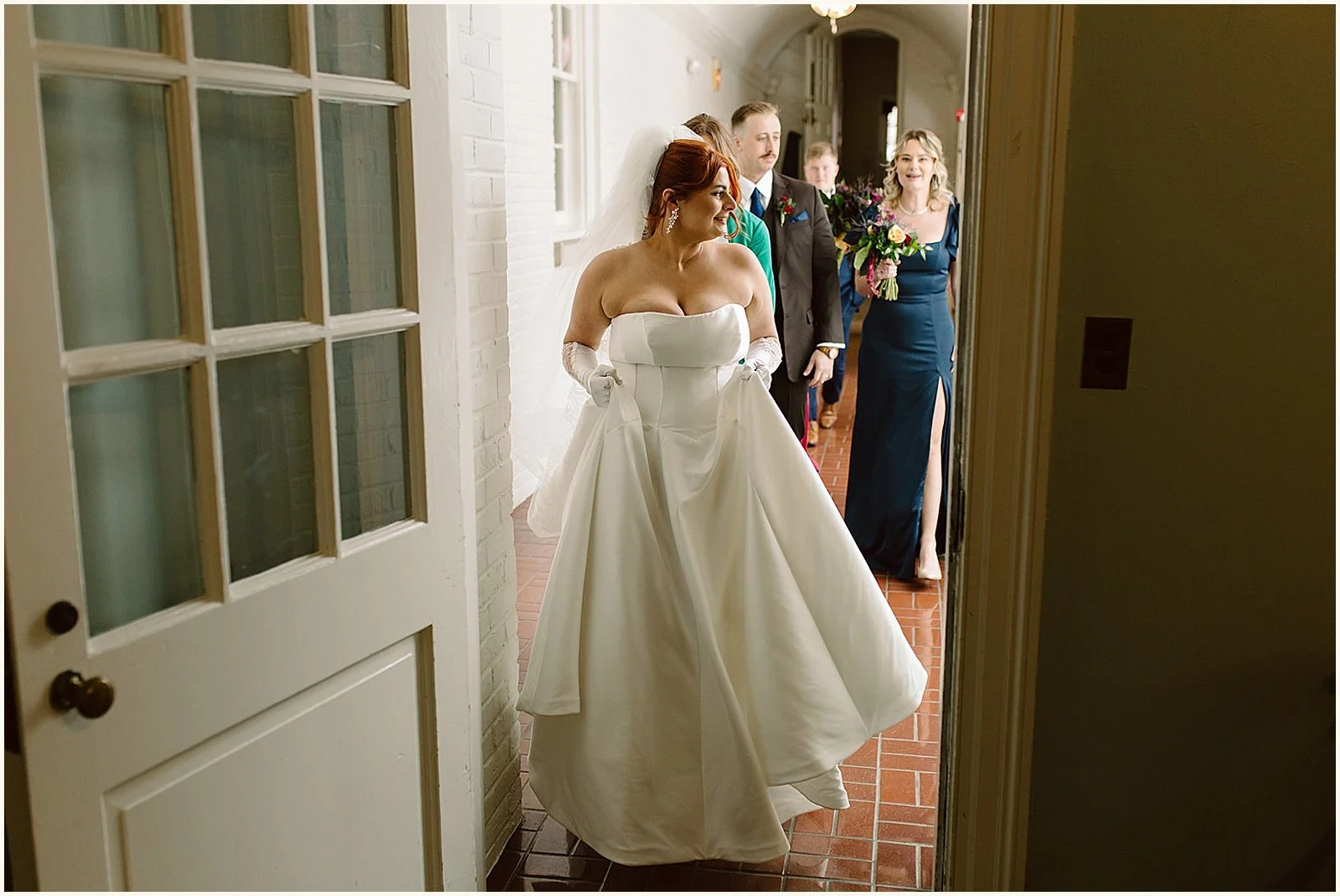 A bride leads a groom and bridesmaids down a sunny hallway.