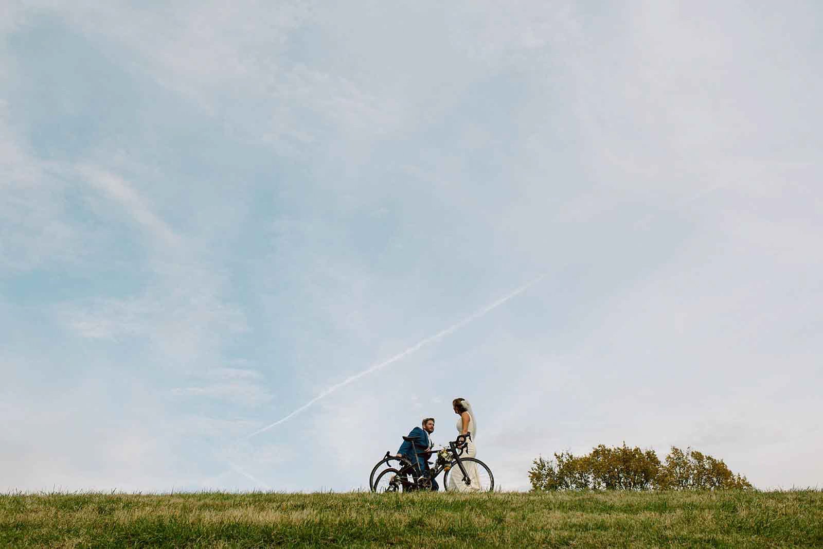A man and woman with bicycles in a grassy field under a partly cloudy sky.