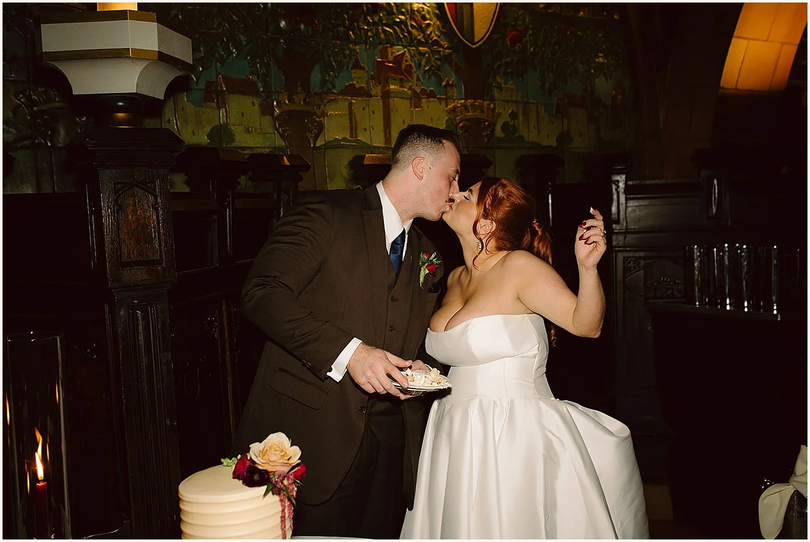 A groom holding a slice of cake kisses a bride.