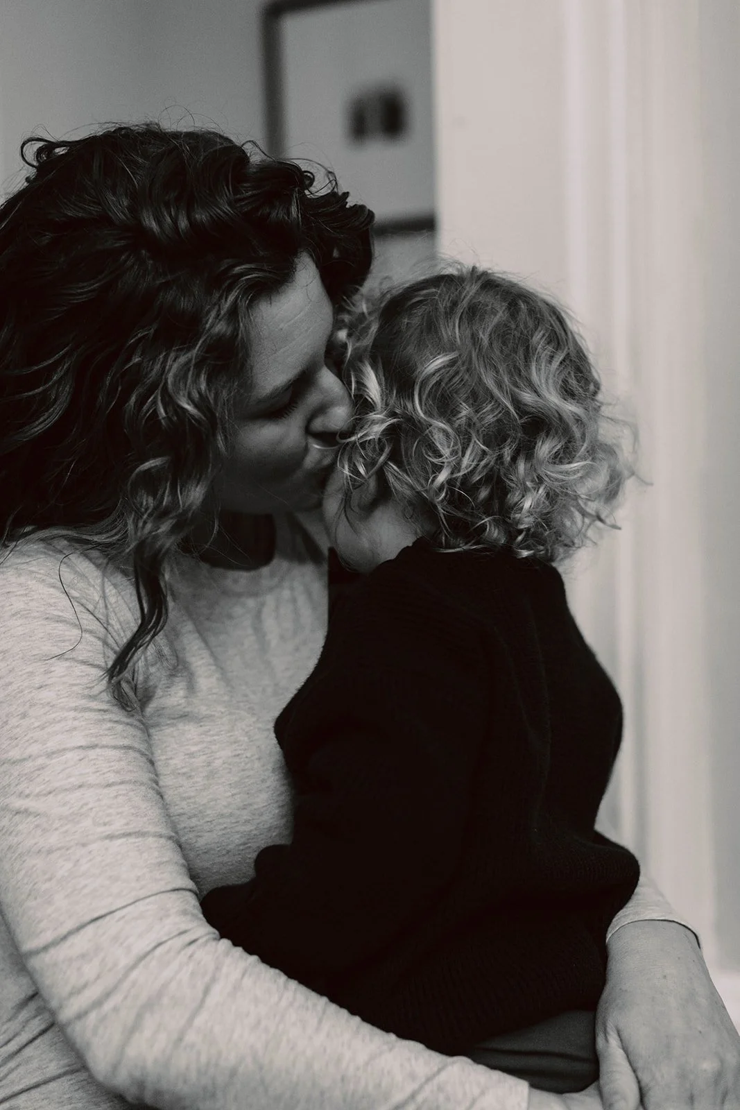 A woman with curly hair kisses a young child with blonde curly hair.