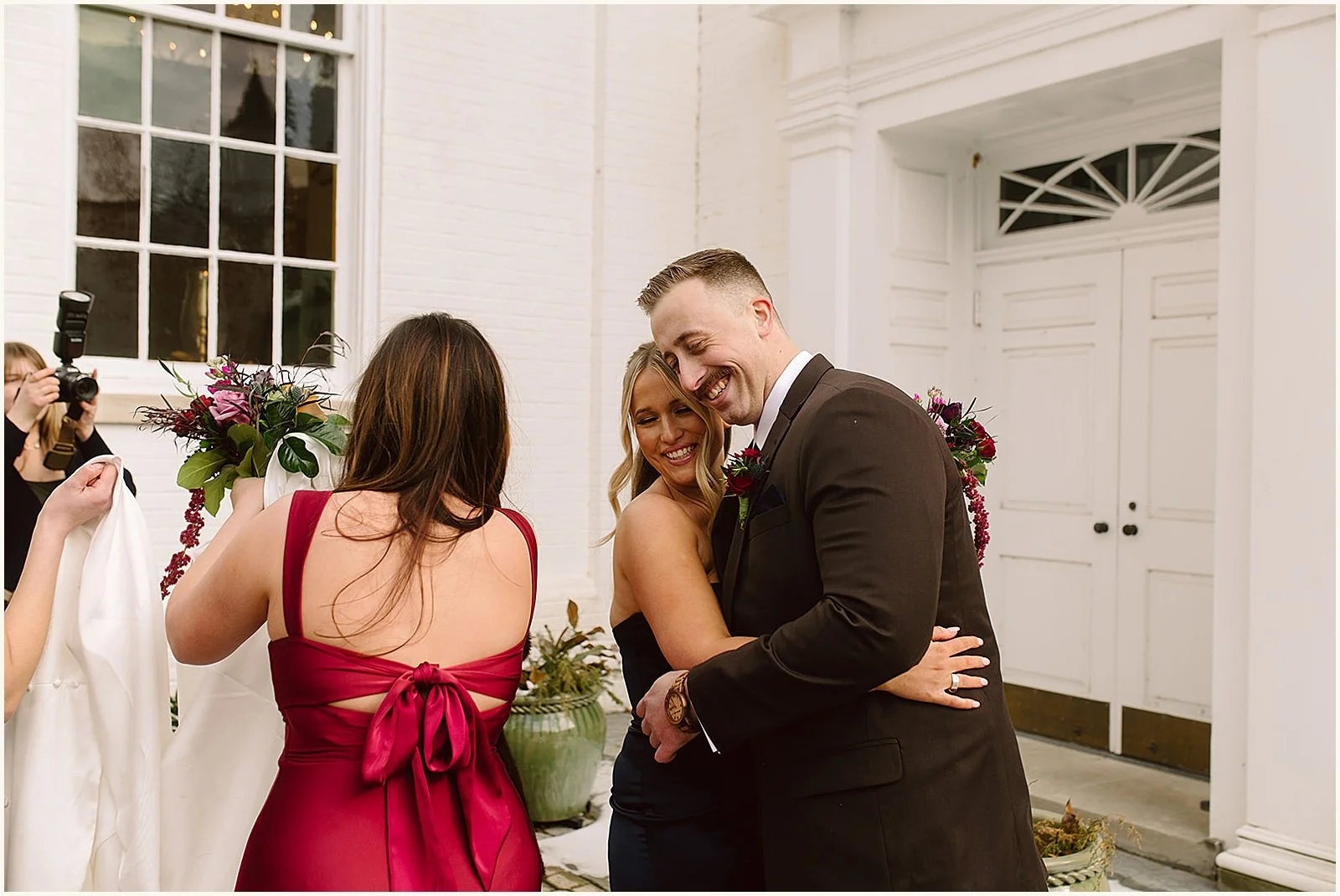 A groom hugs a bridesmaid outside a church.