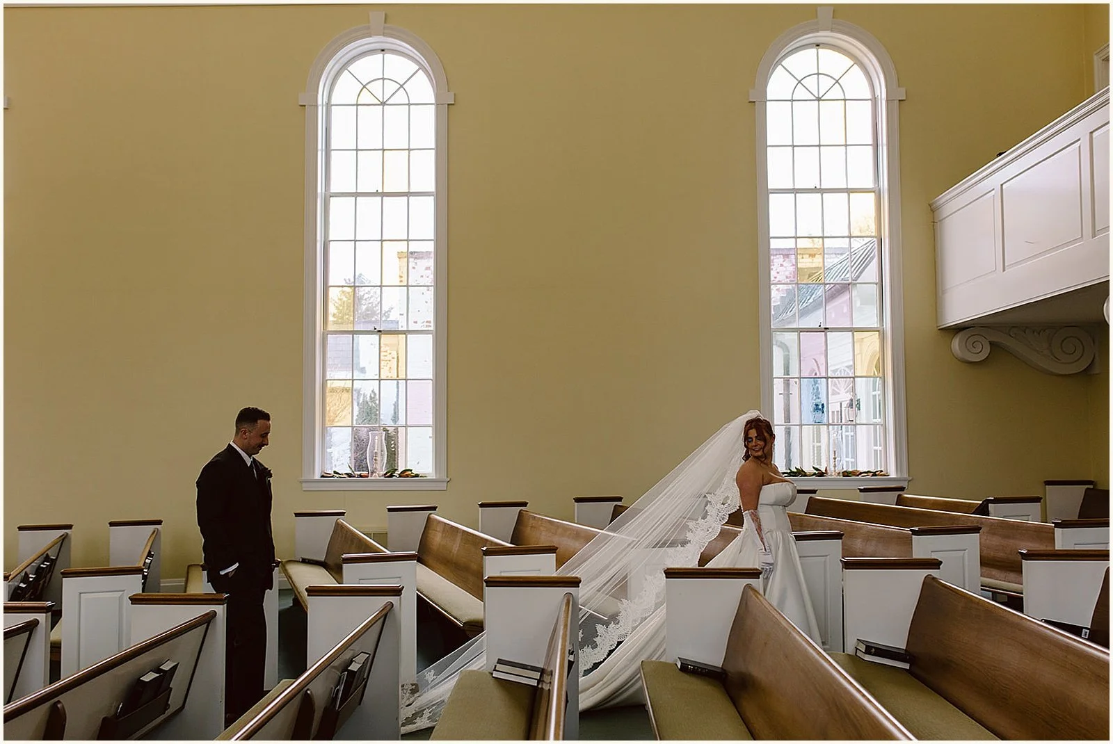 A bride in a long veil poses for a Louisville wedding photographer in an empty church.
