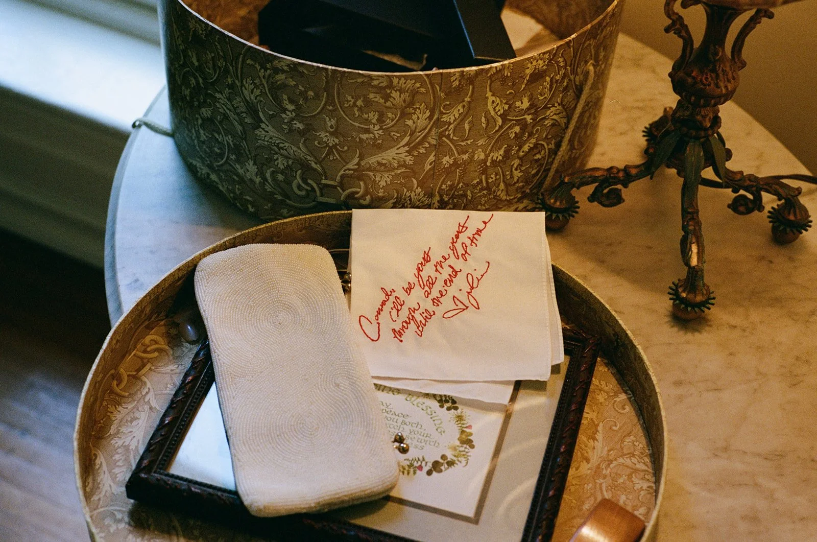 A decorative box on a table containing a white cloth napkin, a pen, a printed card with a Christmas wreath design, and a handwritten note that says 'Enough will be enough tonight, little brother. Love.'
