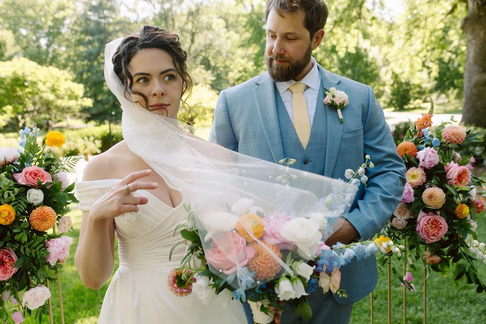 A bride and groom at an outdoor wedding ceremony surrounded by colorful flowers and greenery.