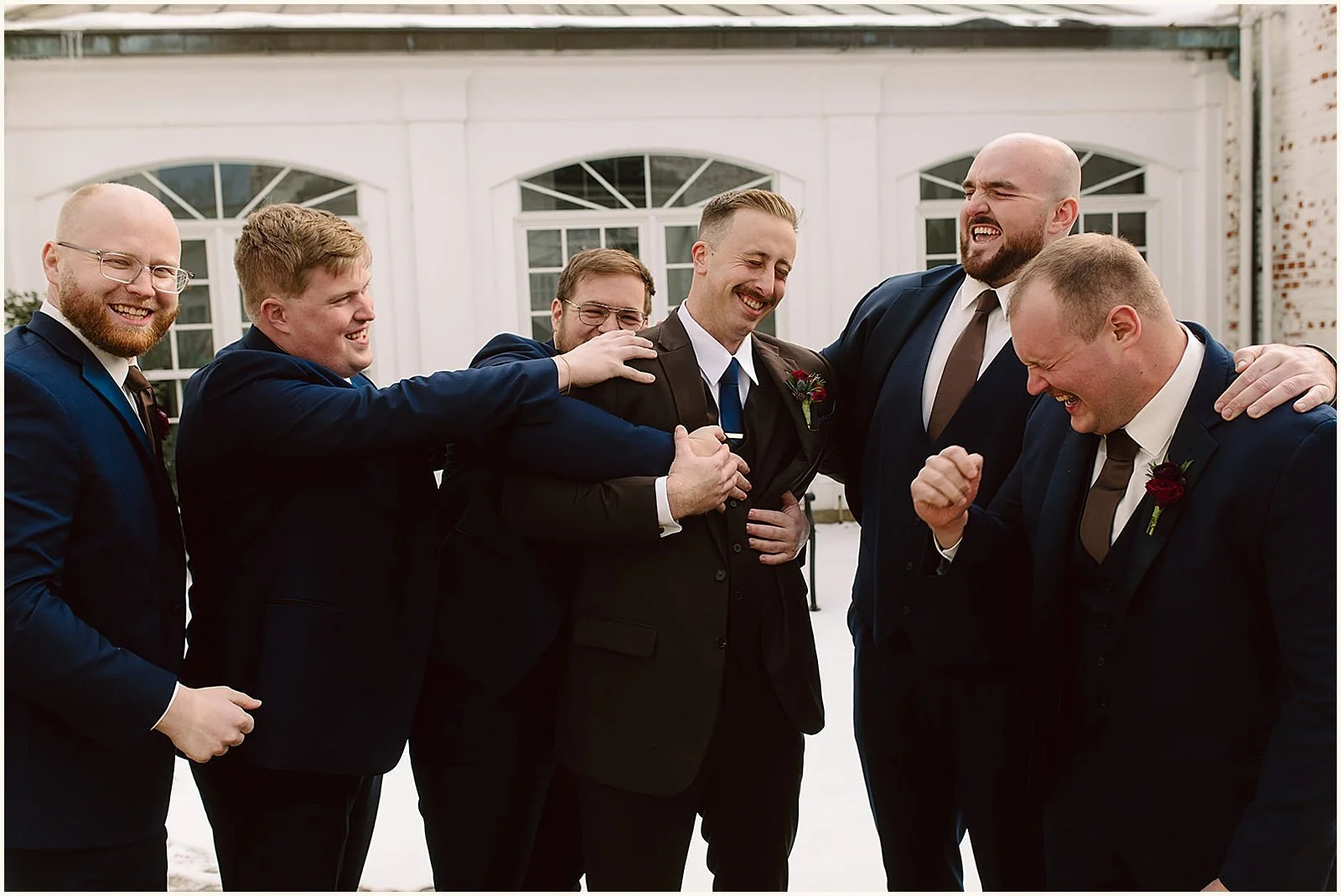 Groomsmen laugh and pat a groom on the shoulders.