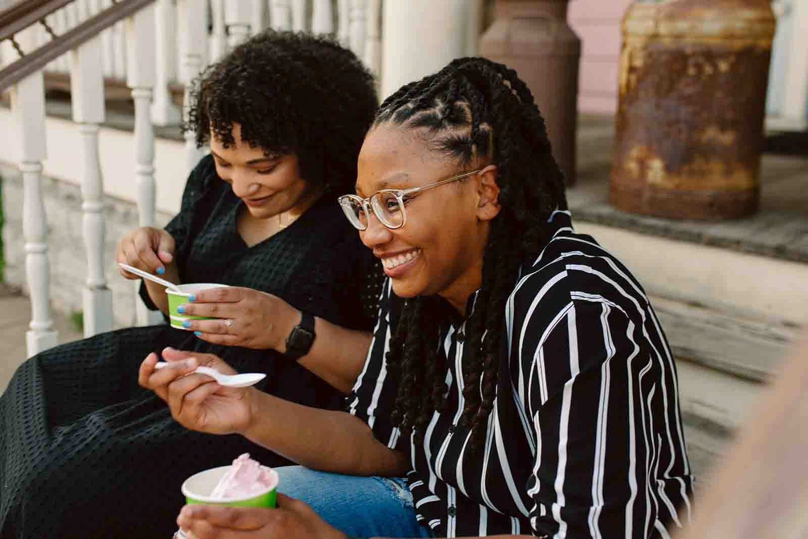 Two women sitting on a porch, smiling and enjoying ice cream from small cups.