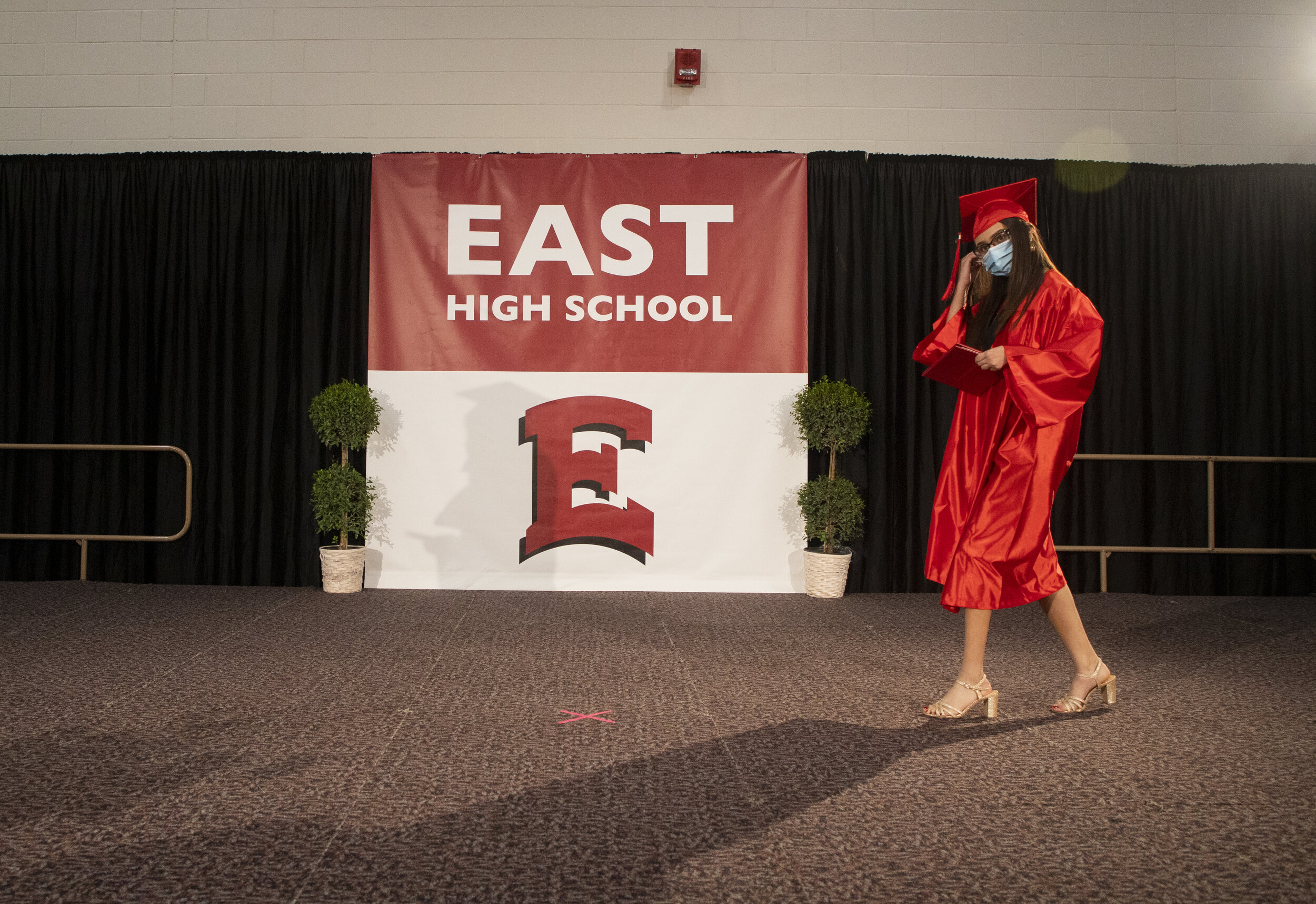  A graduate adjusts her mask as she walks across the stage at East High School's socially distant commencement ceremony on Saturday, June 13, 2020. 