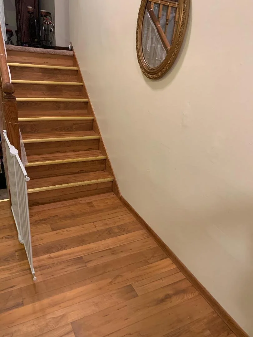 Wooden staircase with a beige wall and a mirror on the wall reflecting part of the staircase and handrail.