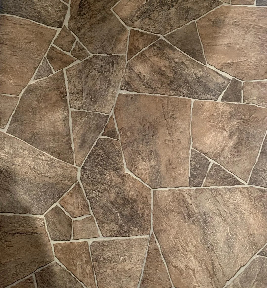 Close-up of a tiled stone wall with irregularly shaped stones in shades of brown and gray, separated by light-colored grout lines.