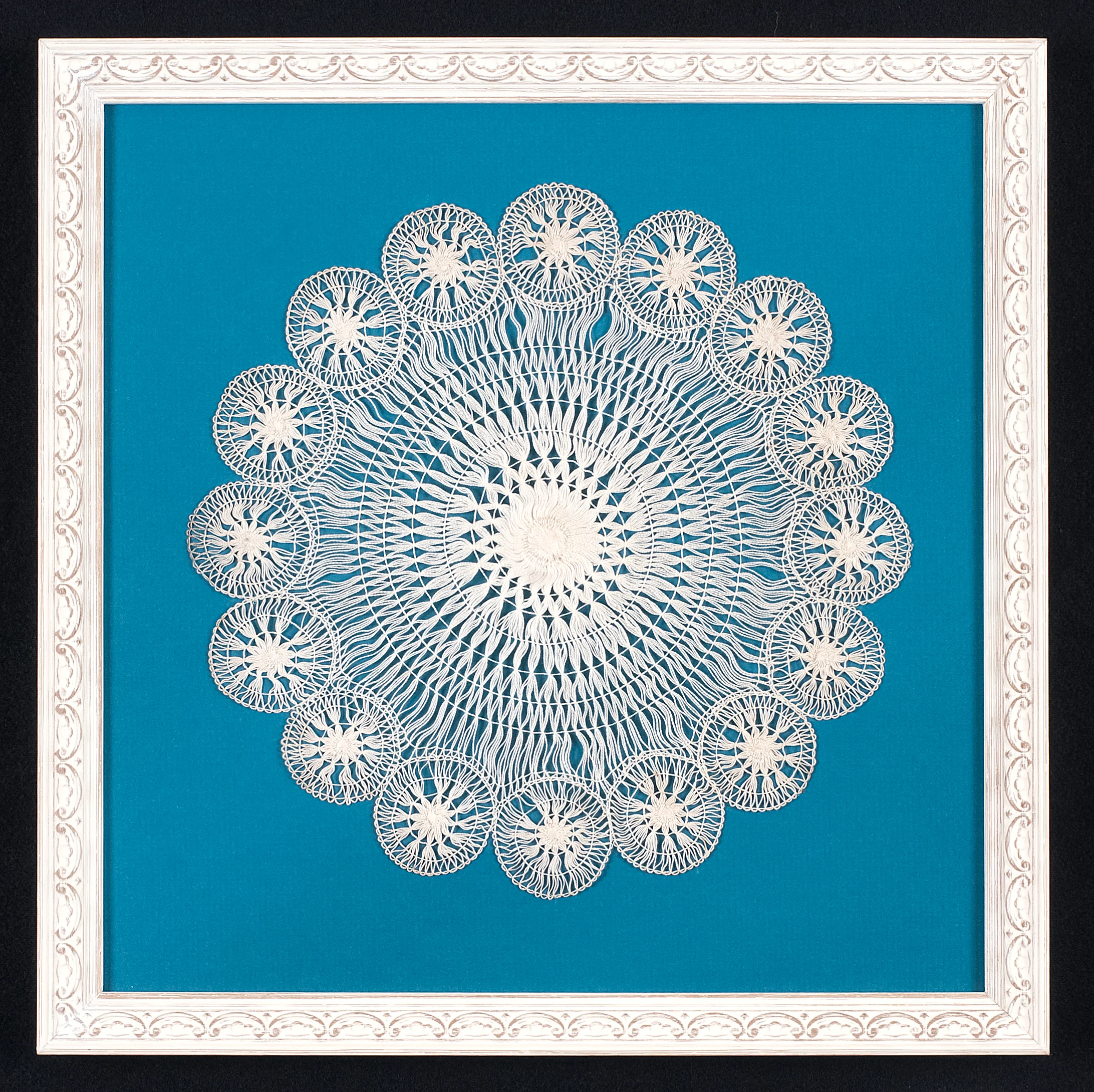  This doily is hand stitched to an acid free mat.Glass spacers are used to lift the ultra violet protective glass off the surface.The frame is a white painted moulding with a floral design. Photo Credit: Elizabeth LaJeunesse .