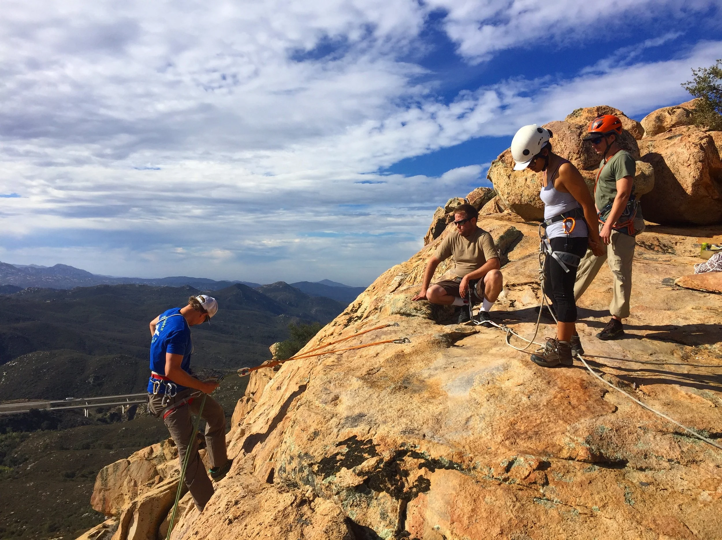 AAC Instructors Piotr An (blue shirt) and Tom Vokes (orange helmet) discuss rappelling basics with AAC Members Toby Hutchens and Melissa Angeles. Photo cred: Jonathan Wachtel