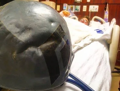 Gorder in the hospital with the dented helmet that he believes saved his life or prevented a serious head injury.