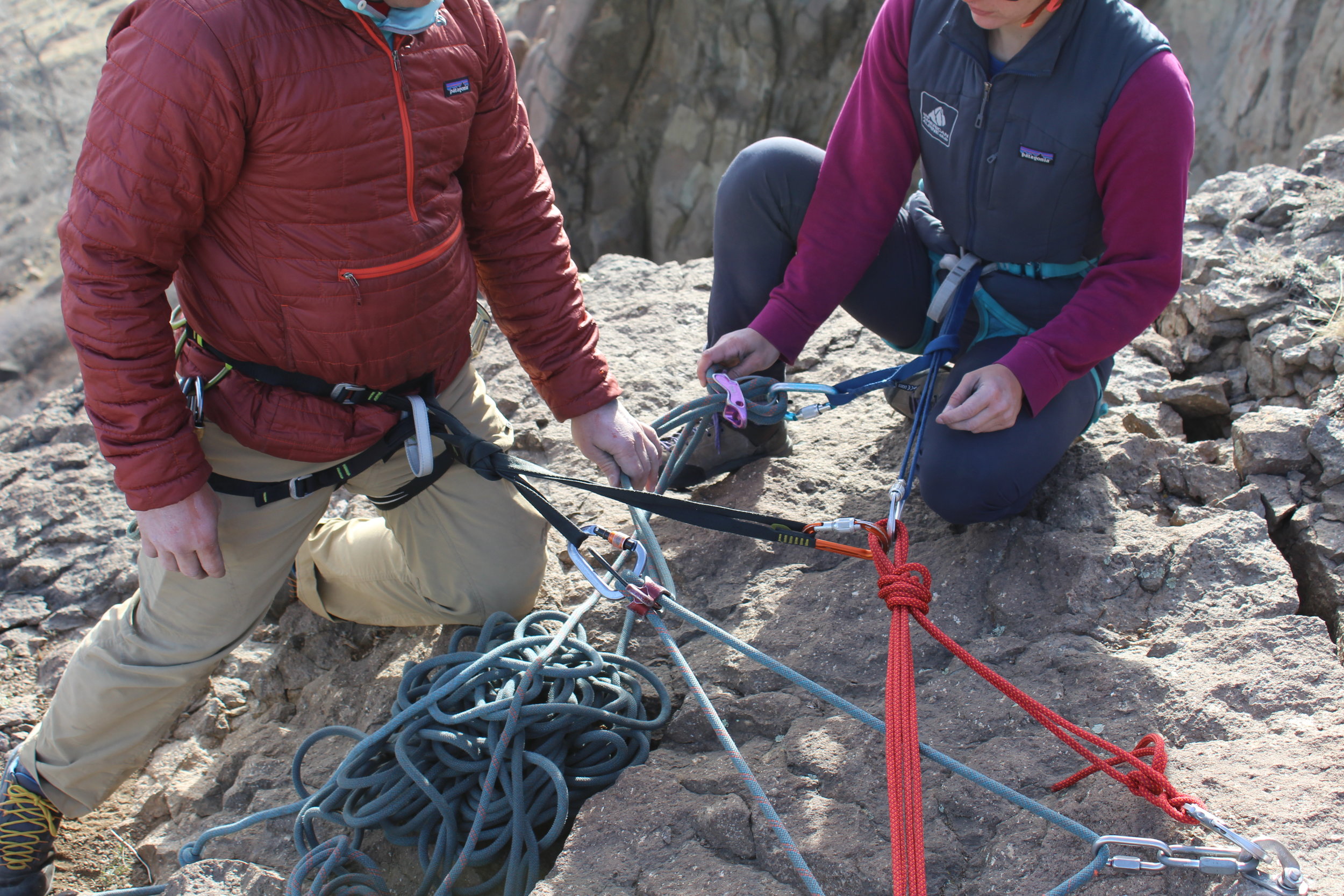 With their back turned towards a precipitous cliff's edge and their attention focused on setup tasks, these climbers are using technical security (a tether and locking carabiner) to stay secured during setup.&nbsp;
