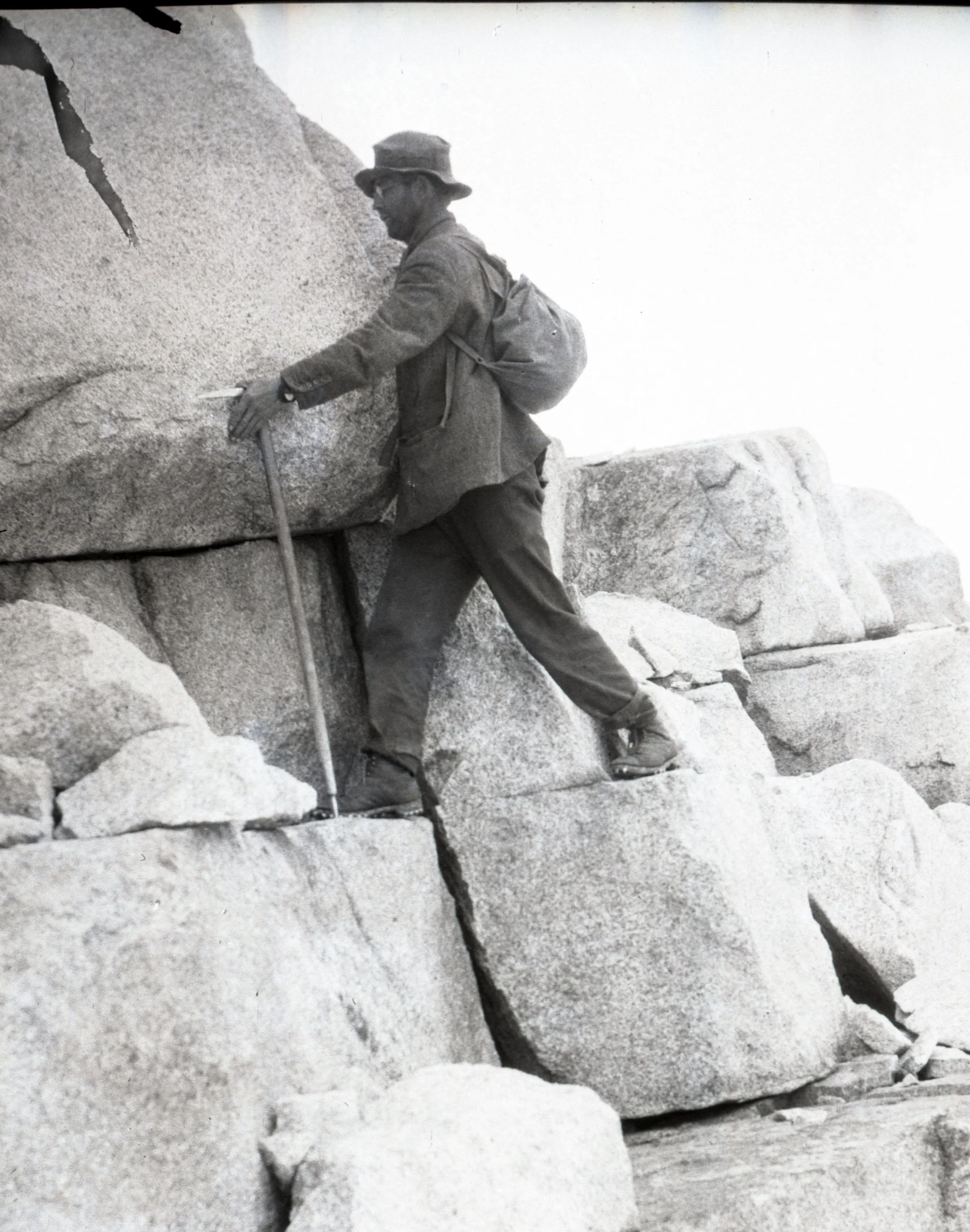 A climber ascending a rock face, using his ice axe as a walking stick. From the collections of the American Alpine Club.