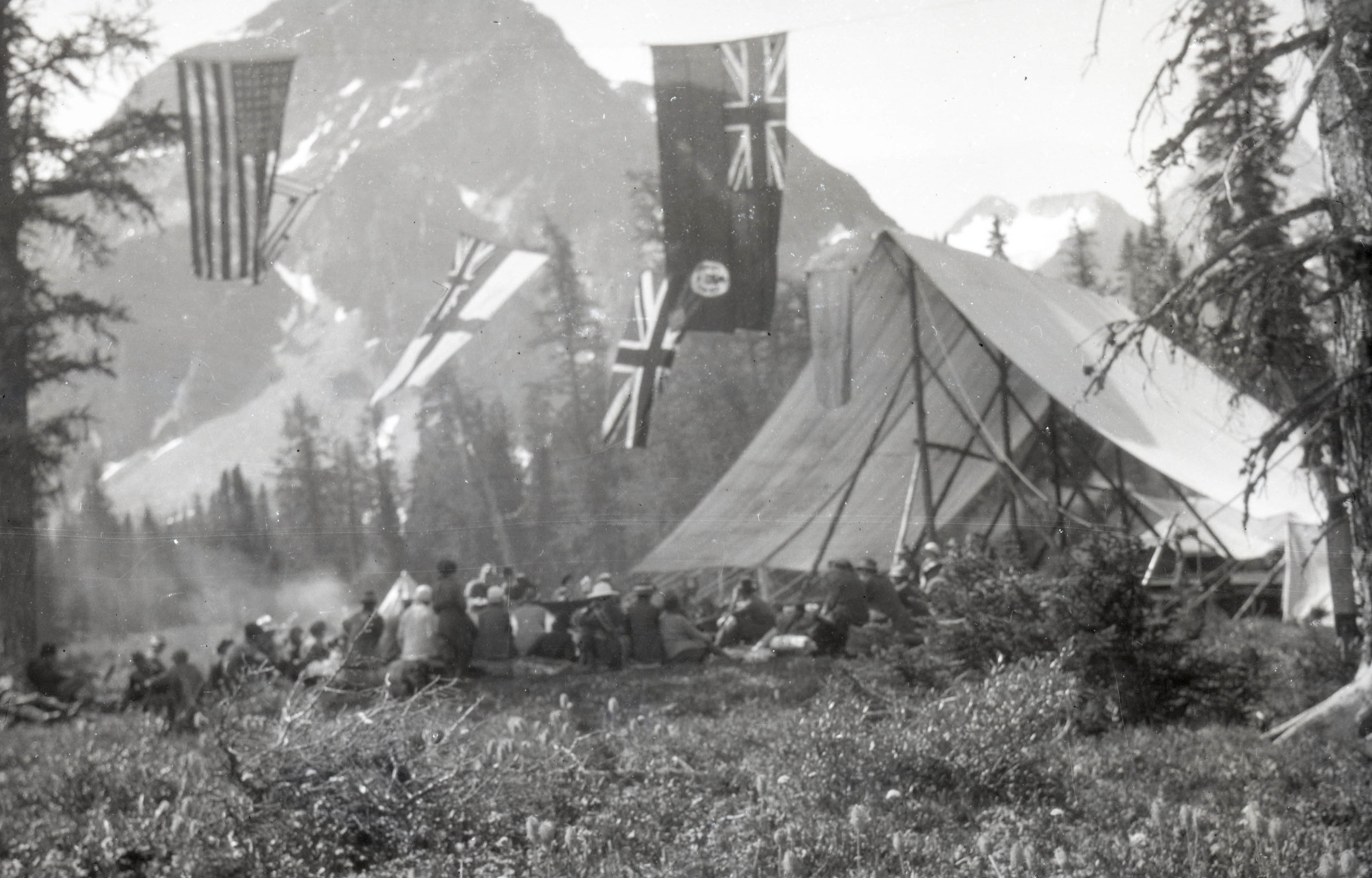  A mess tent and a large group of people around a campfire under US and Canadian flags 