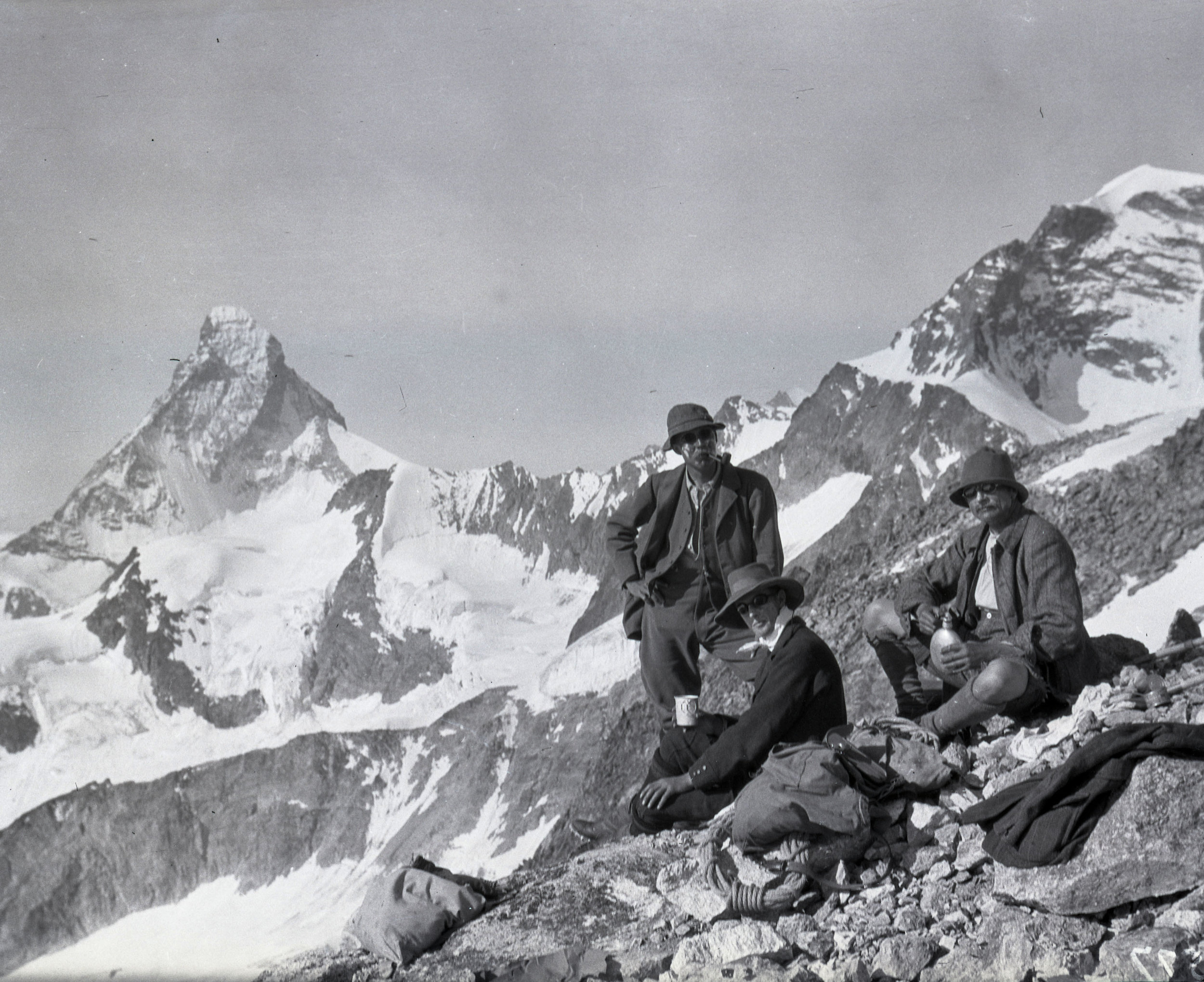  Three men pause for refreshment while climbing in the Alps. The Matterhorn in the background. 