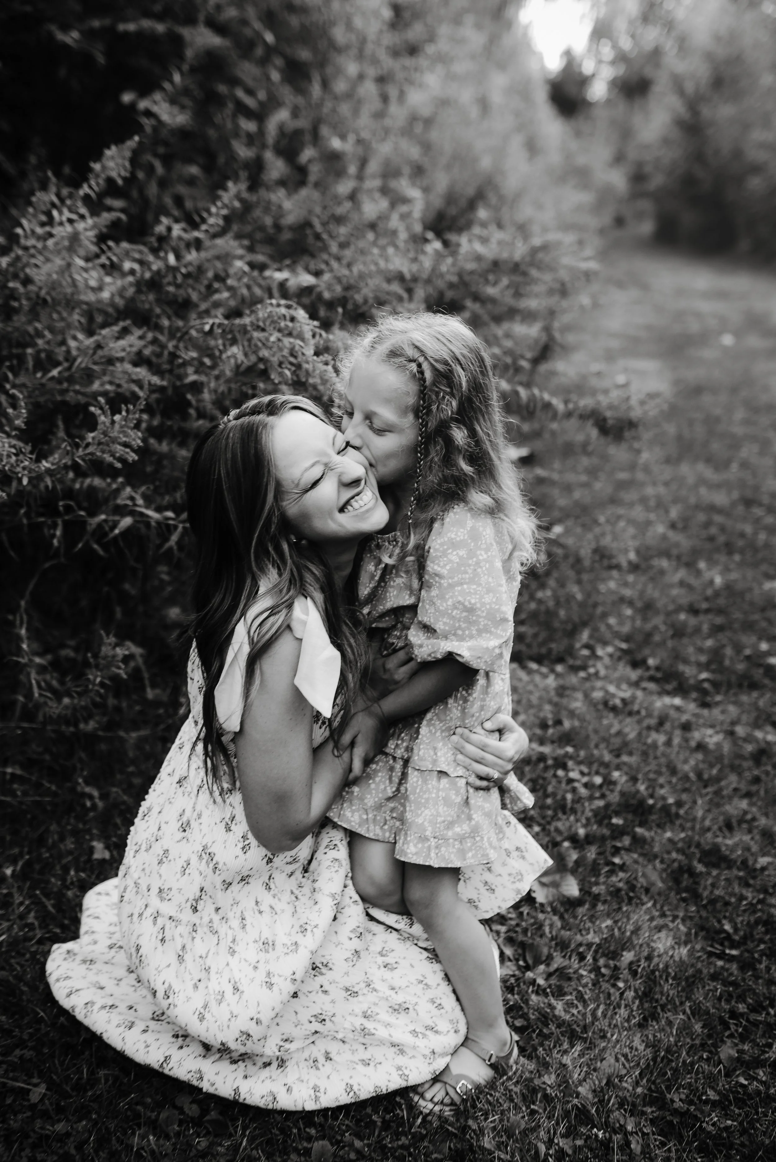 A woman and a young girl sharing a joyful moment outdoors, with the girl kissing the woman on the cheek.