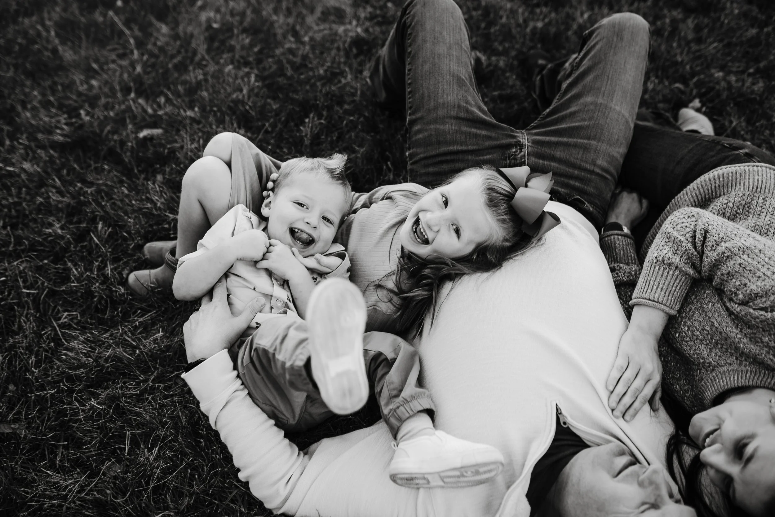 A woman and three children lying on the grass, all smiling and enjoying a moment together.