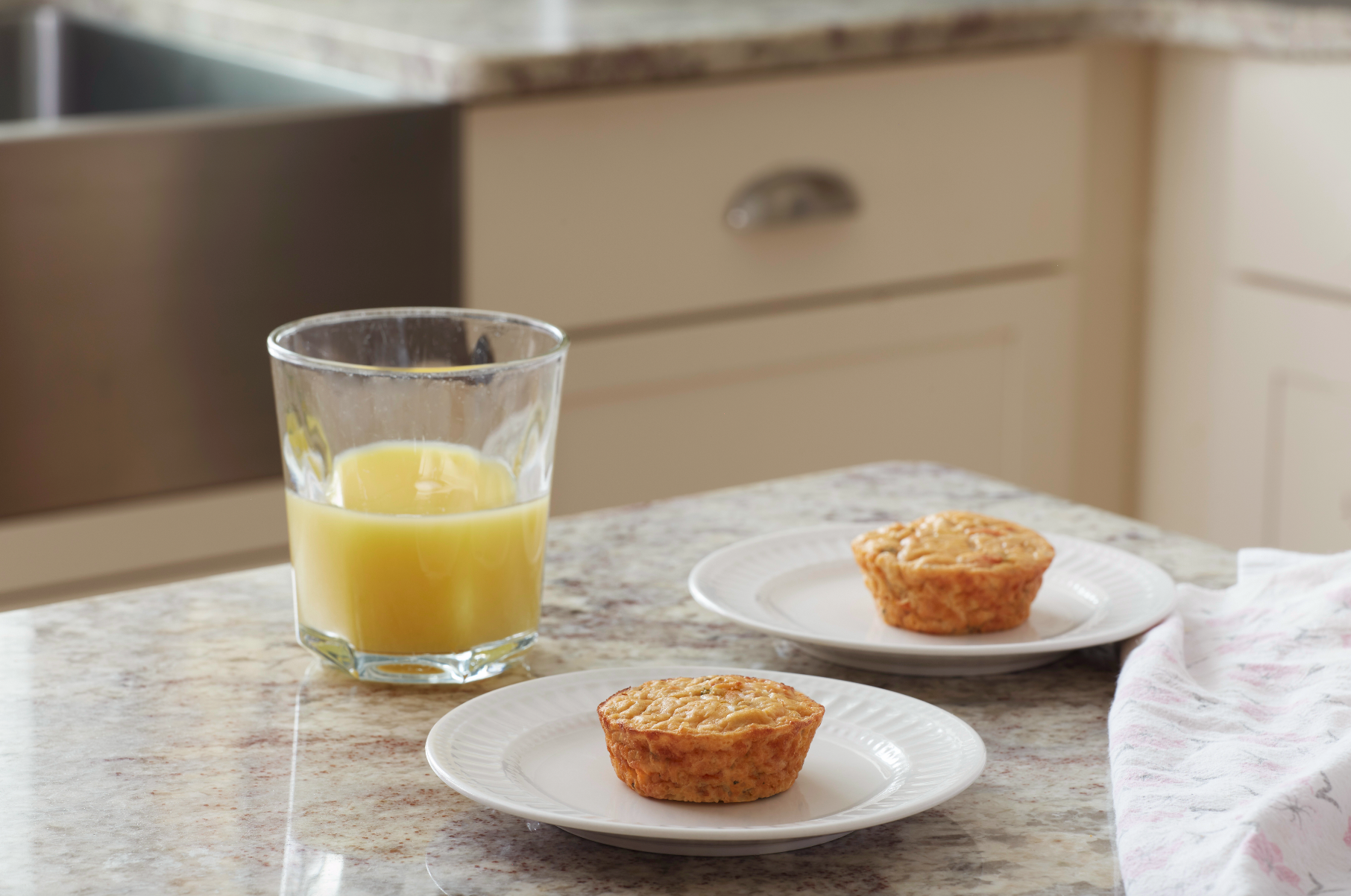 two plates with one tomato basil frittata each and a glass of orange juice on a marble kitchen countertop