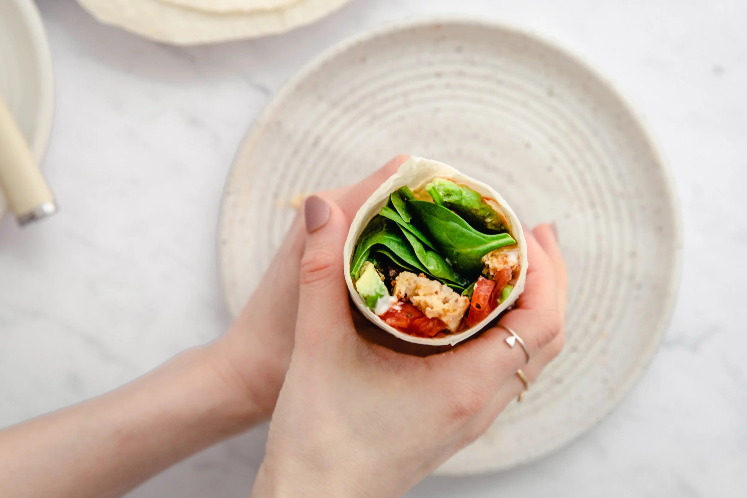 Hand holding frittata breakfast burrito over plate