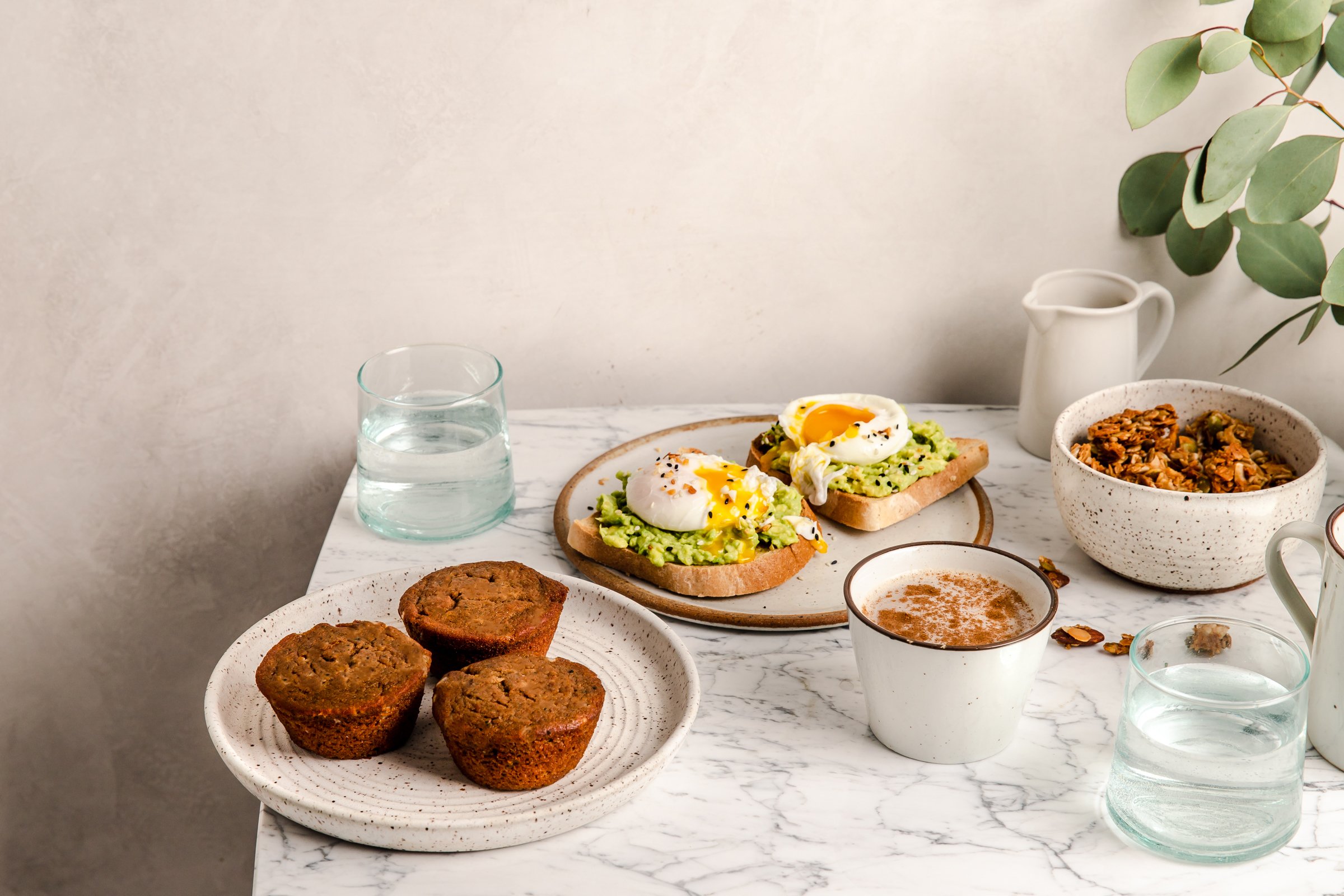 three keto-friendly cinnamon roll muffins on a plate, with another plate featuring two eggs benedict on avocado toast