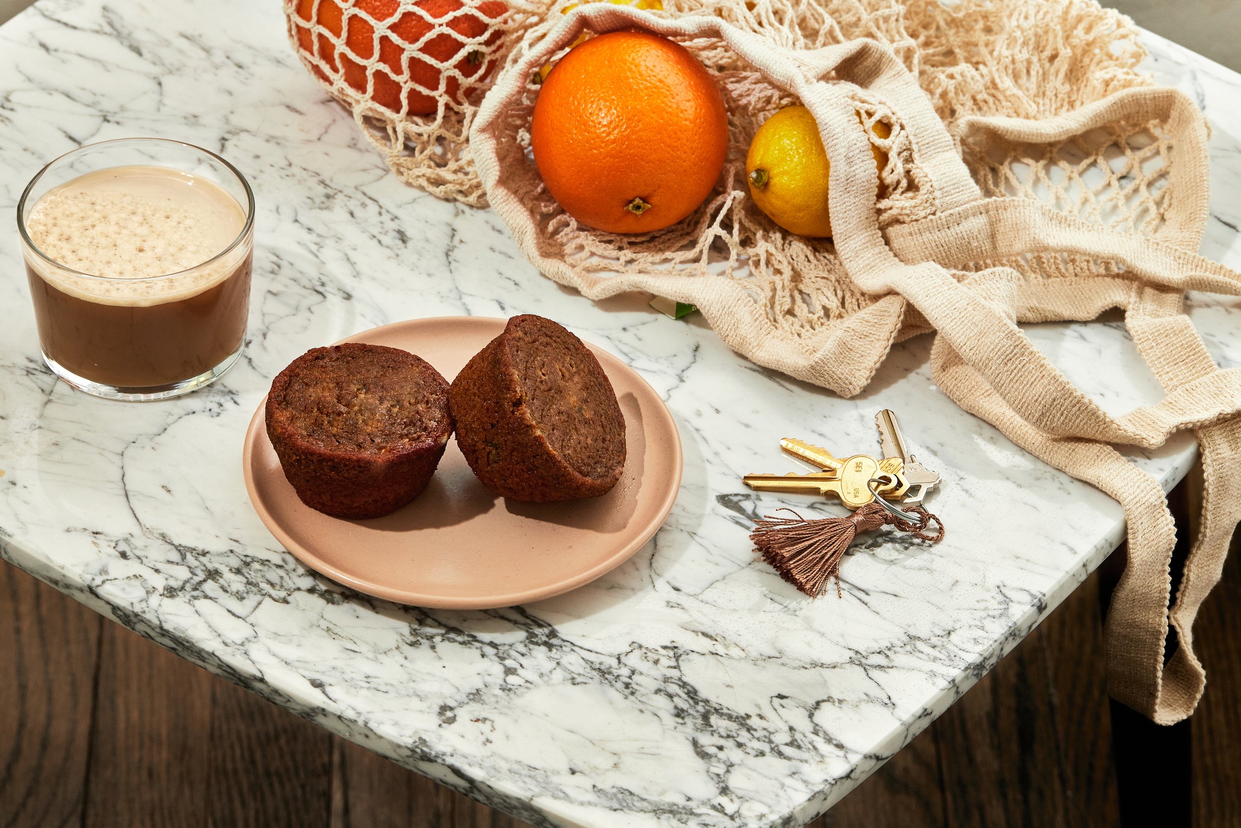 two keto friendly cinnamon roll muffins on a plate, placed on a marble counter in front of a netted bag of citrus fruits