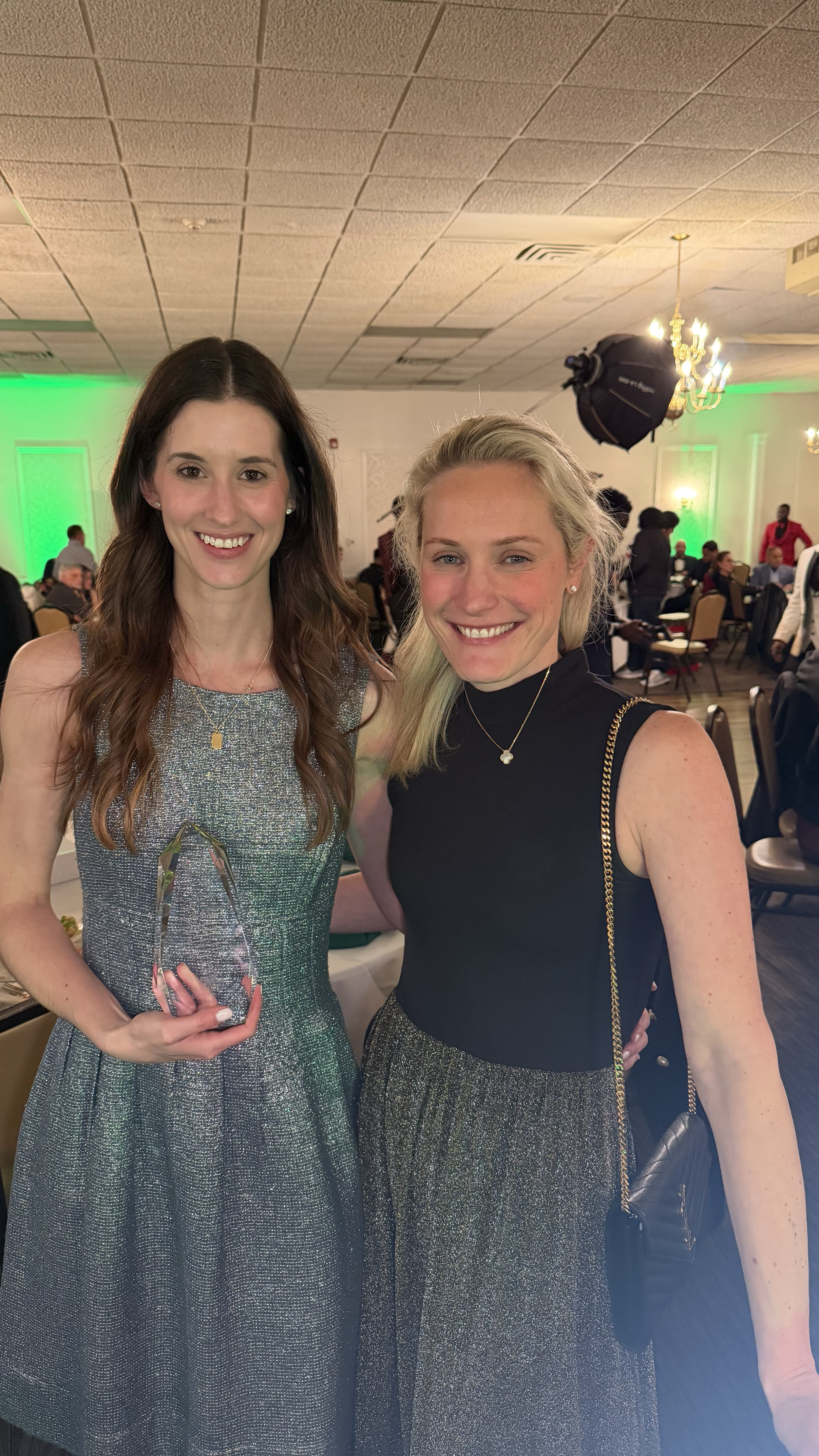 Two women smiling at a celebration event, with one woman holding an award.