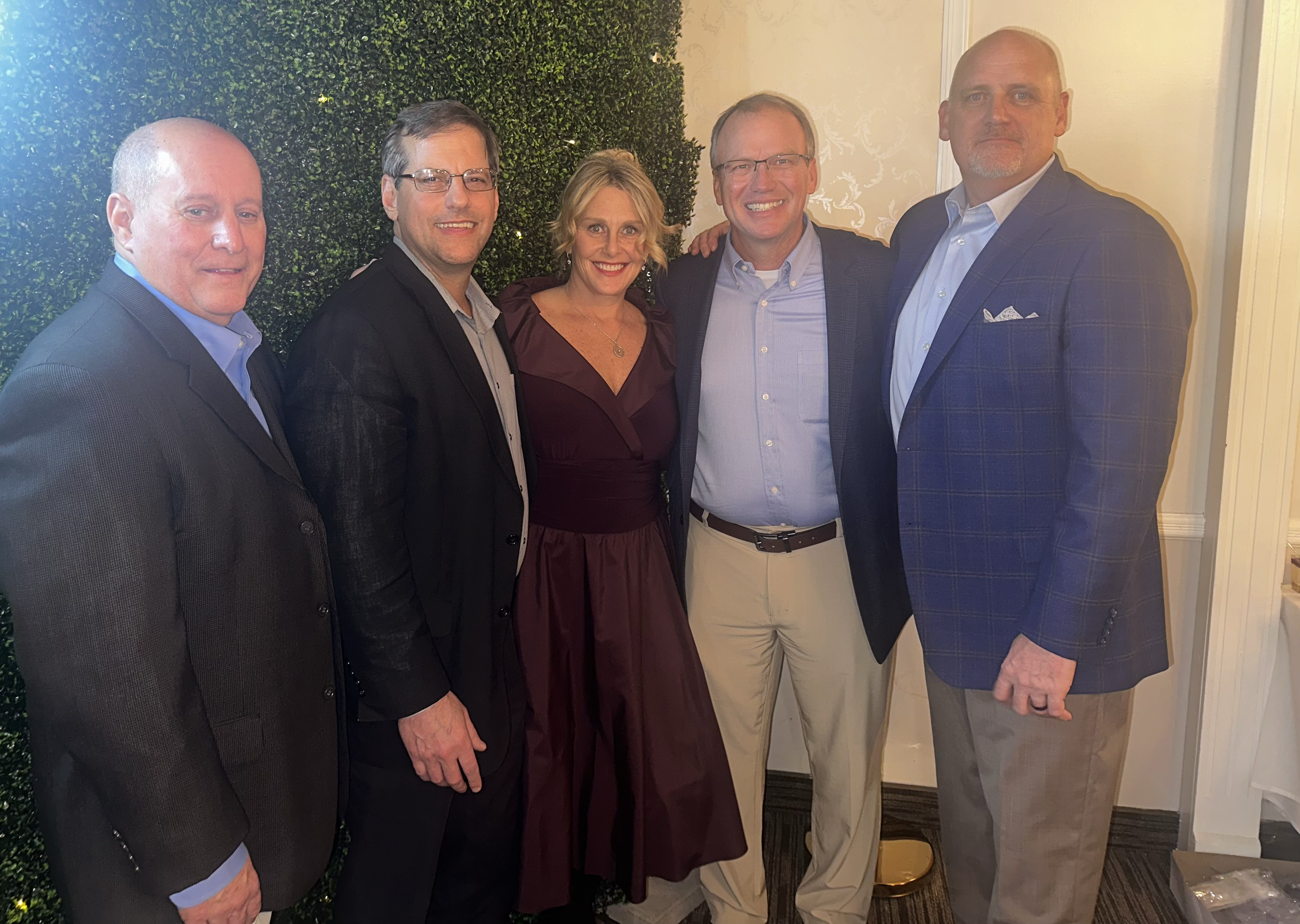 Five people dressed in formal attire standing together indoors, smiling for the photo.