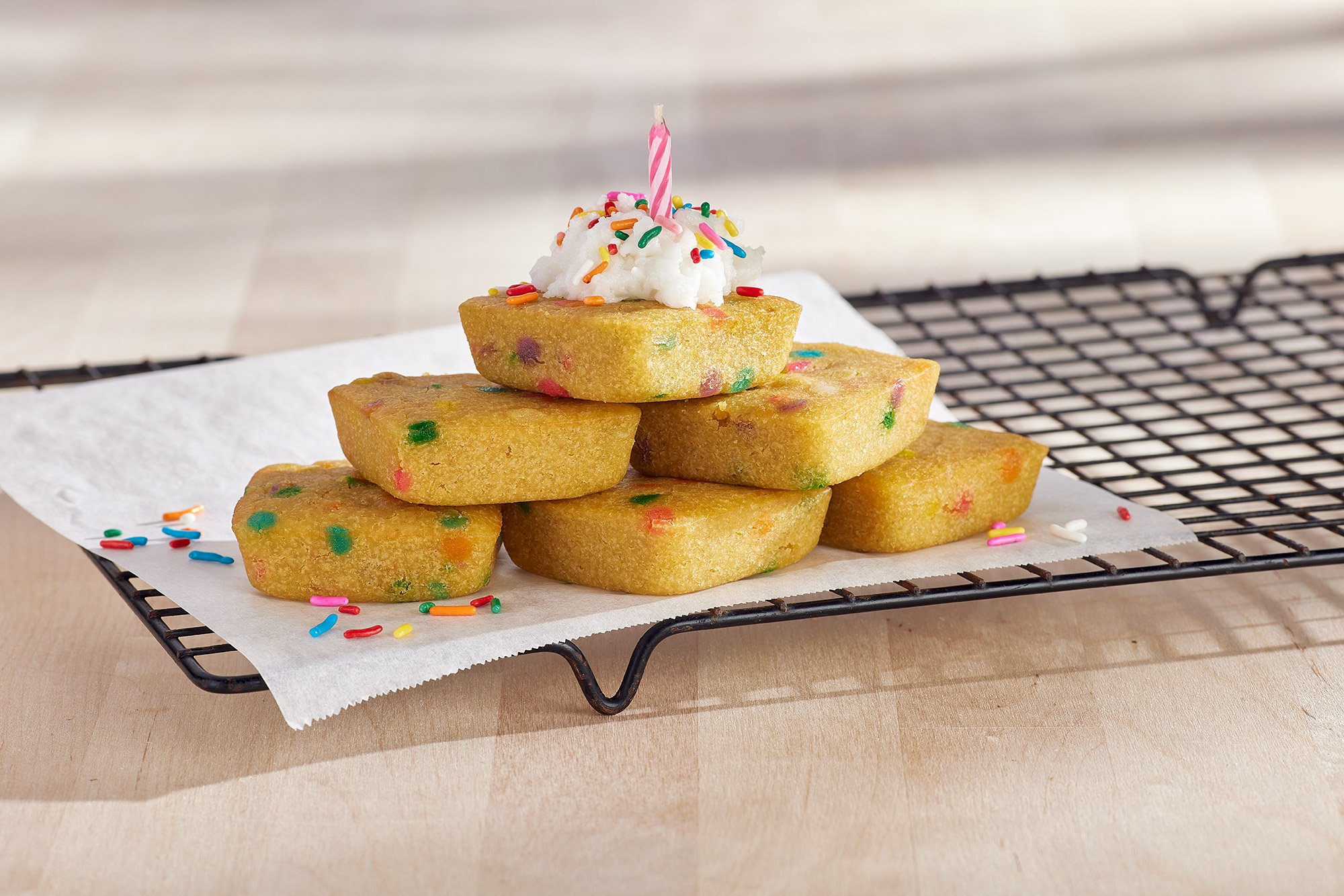 stack of birthday cake brownie bites on a cooling rack with whipped cream and a candle