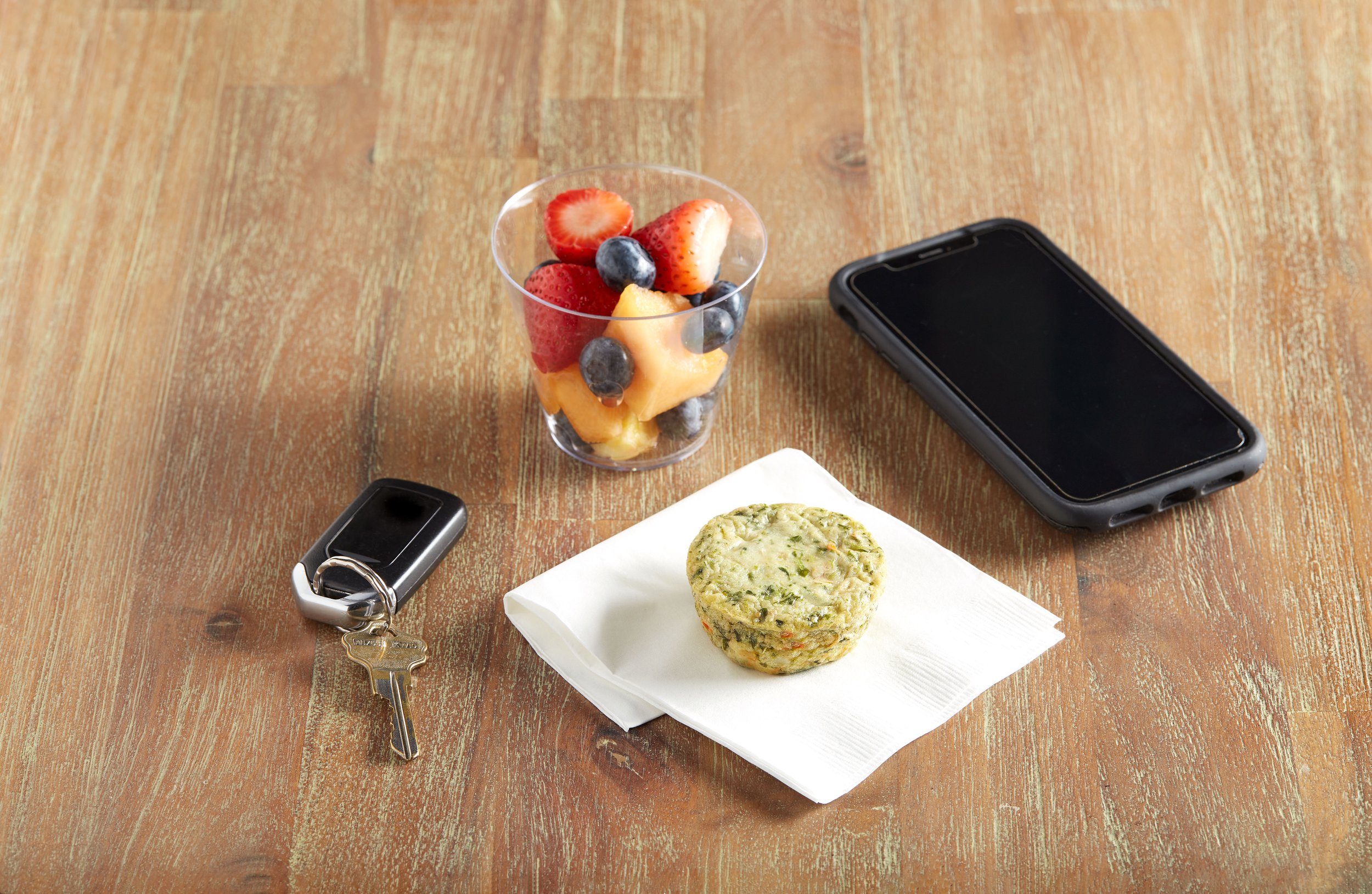 frittata on napkin with phone, keys and fruit cup
