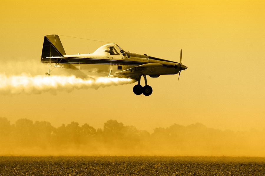 Plane dropping pesticides and herbicides on crops.
