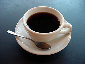 A cup of coffee on a plate with a spoon. Coffee supports and boost the endocannabinoid system.
