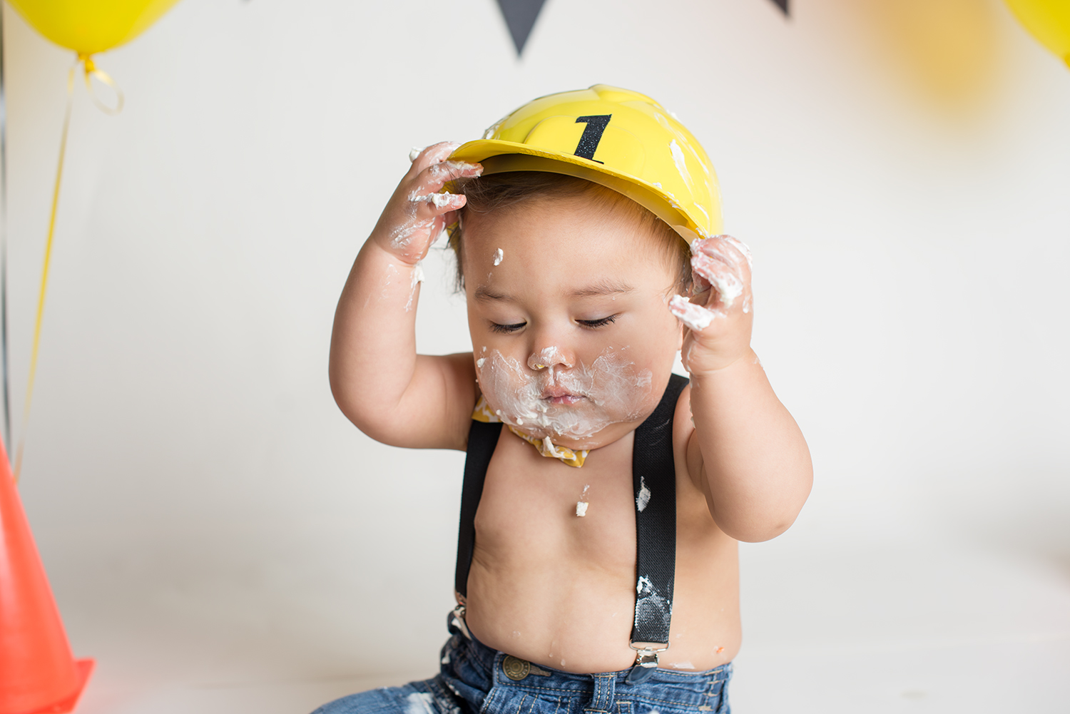 construction theme baby holding hat while eating smash cake