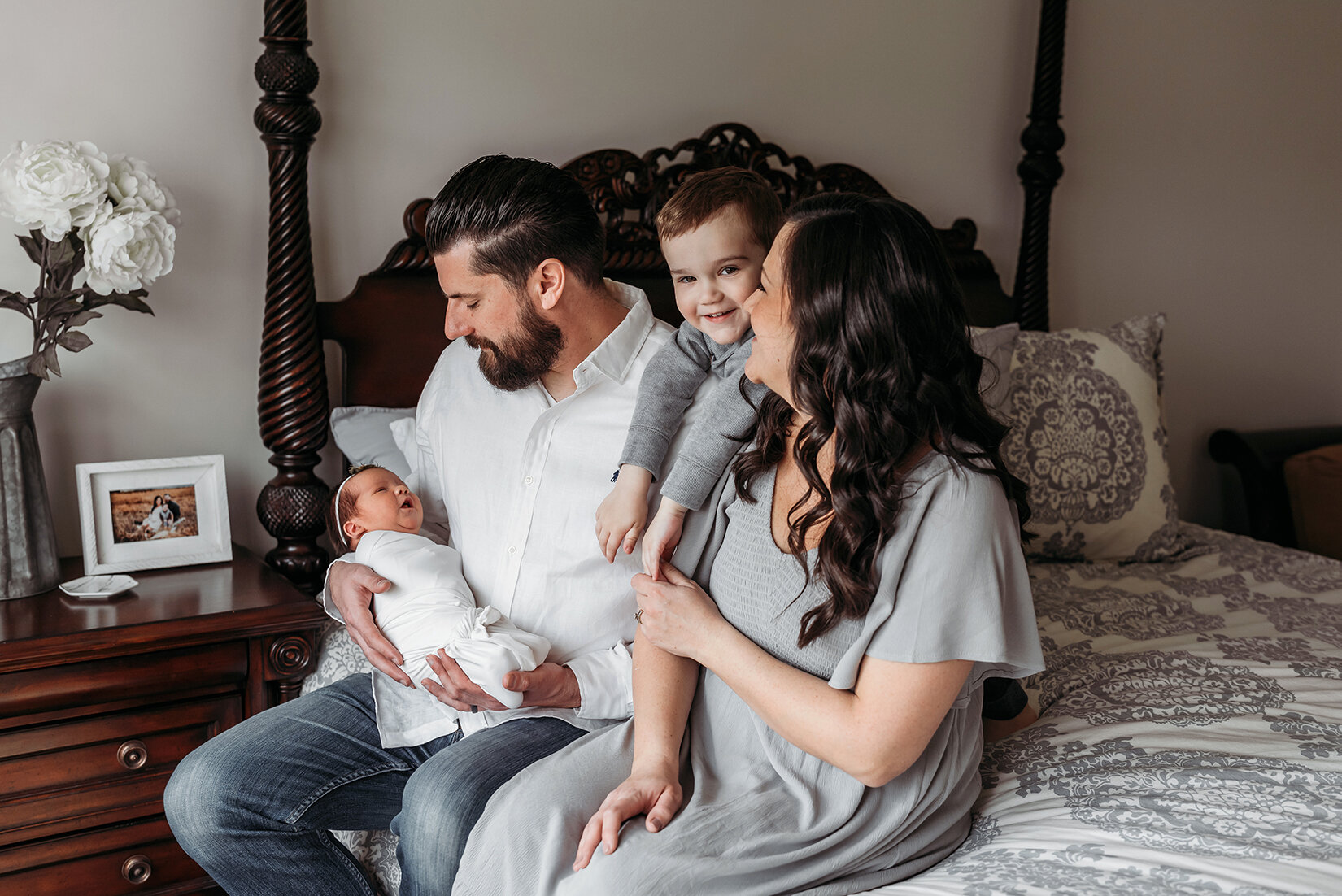 family sitting on edge of bed with their newborn baby.jpg