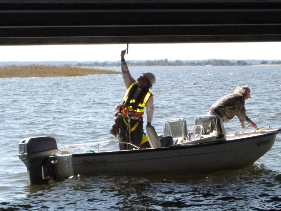 An A&O bridge inspector “sounds the element,” tapping lightly against the bridge structure to identify deficiencies in the concrete. 